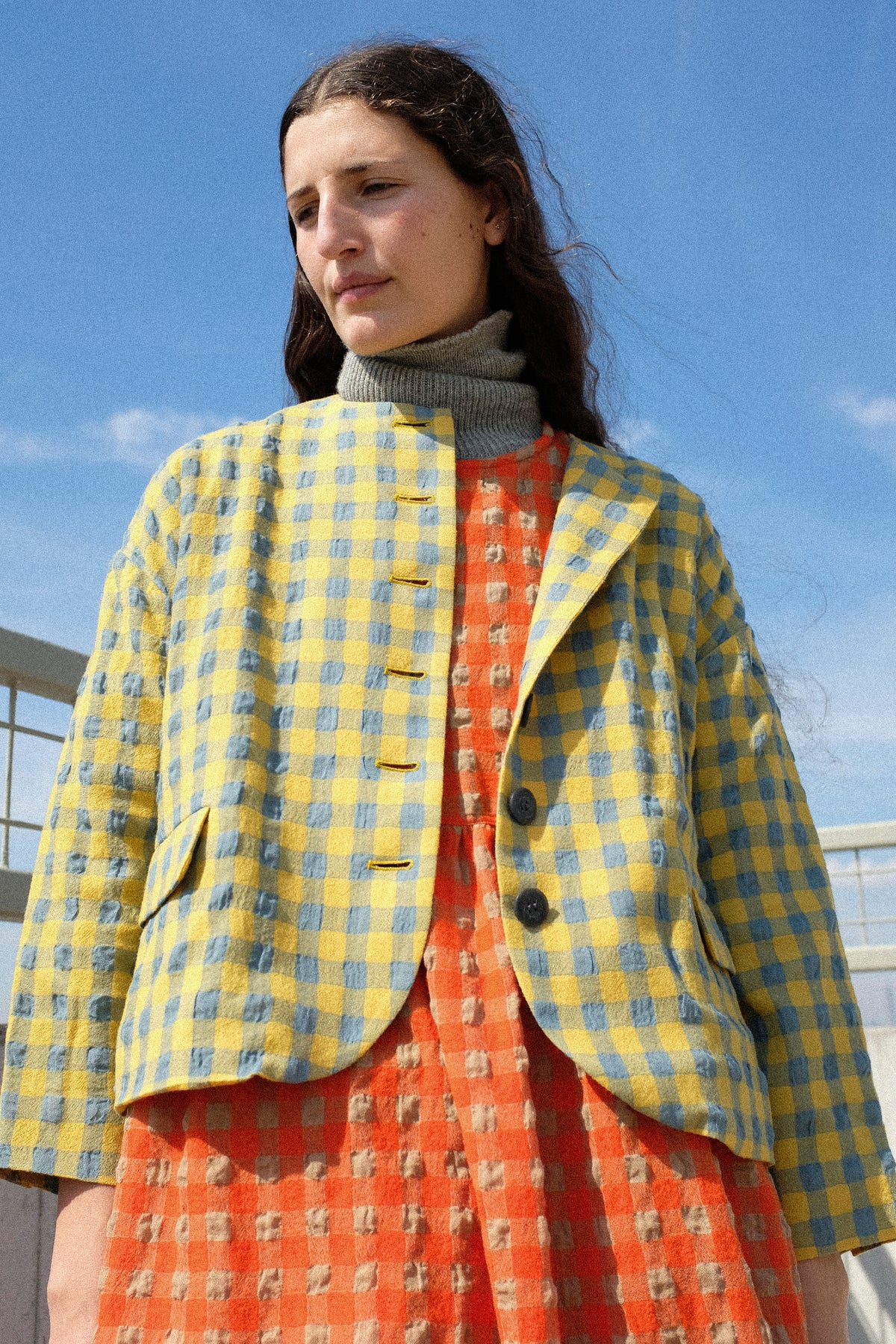 A woman standing outside wearing Ichi Antiquités Gingham Check Jacket in Blue and Yellow, over the Gingham Check Dress in Beige and Orange.