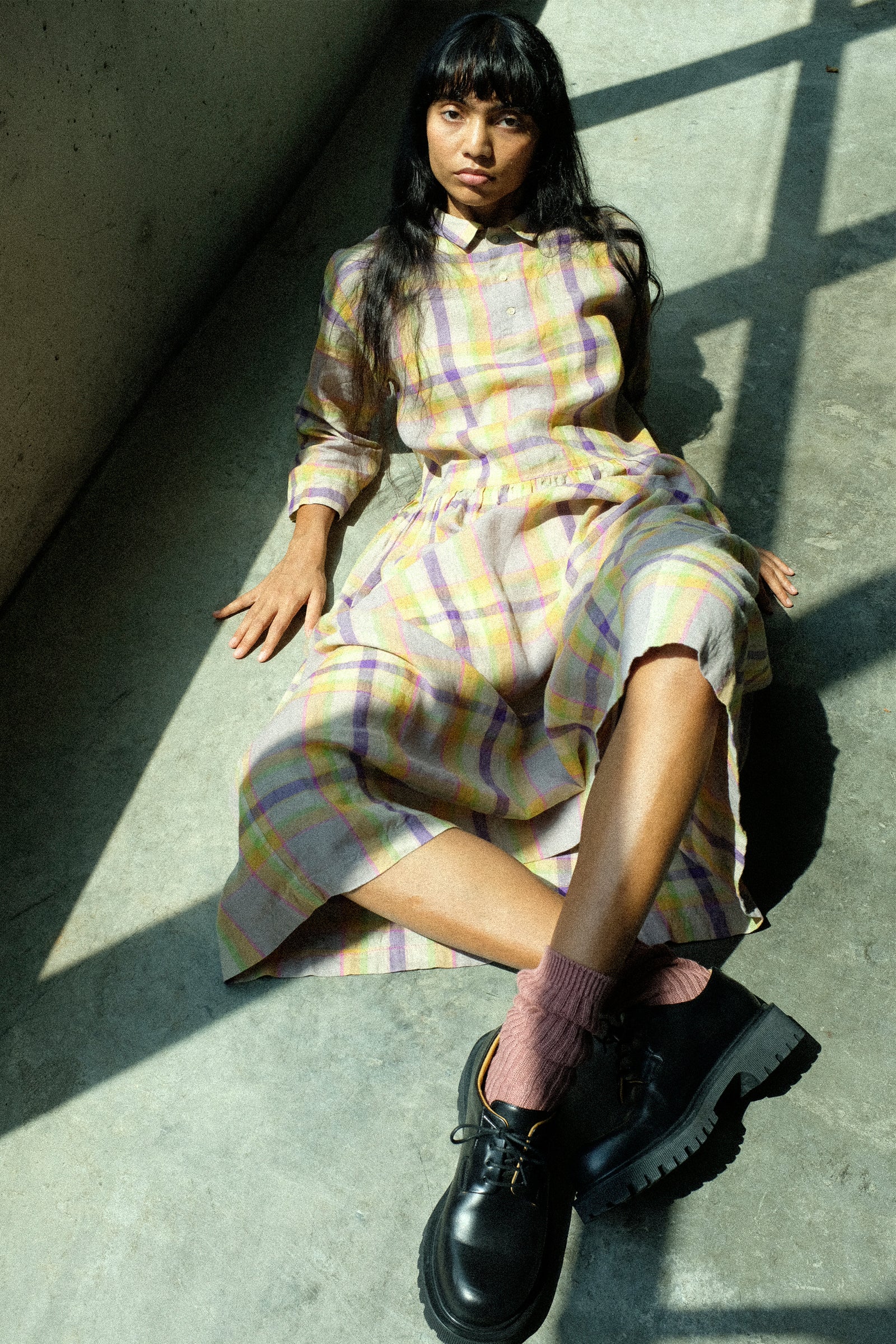 Person wearing an Ichi Antiquites plaid dress with black shoes sitting on a concrete floor.