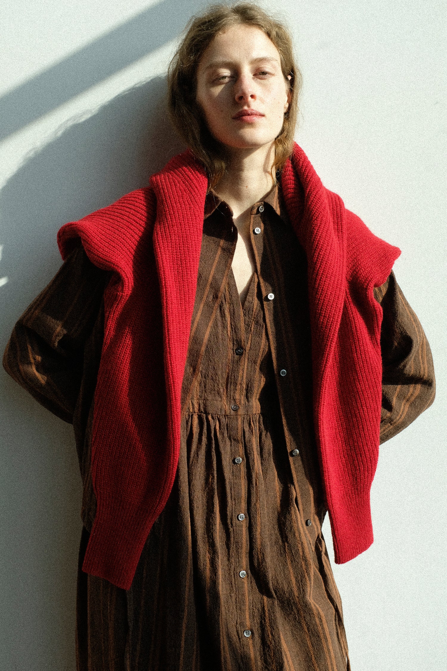 Person wearing the Ichi Antiquités Wool Rib Knit Pullover in Red, and Linen Cotton Random Stripe Dress in Brown against a white wall.