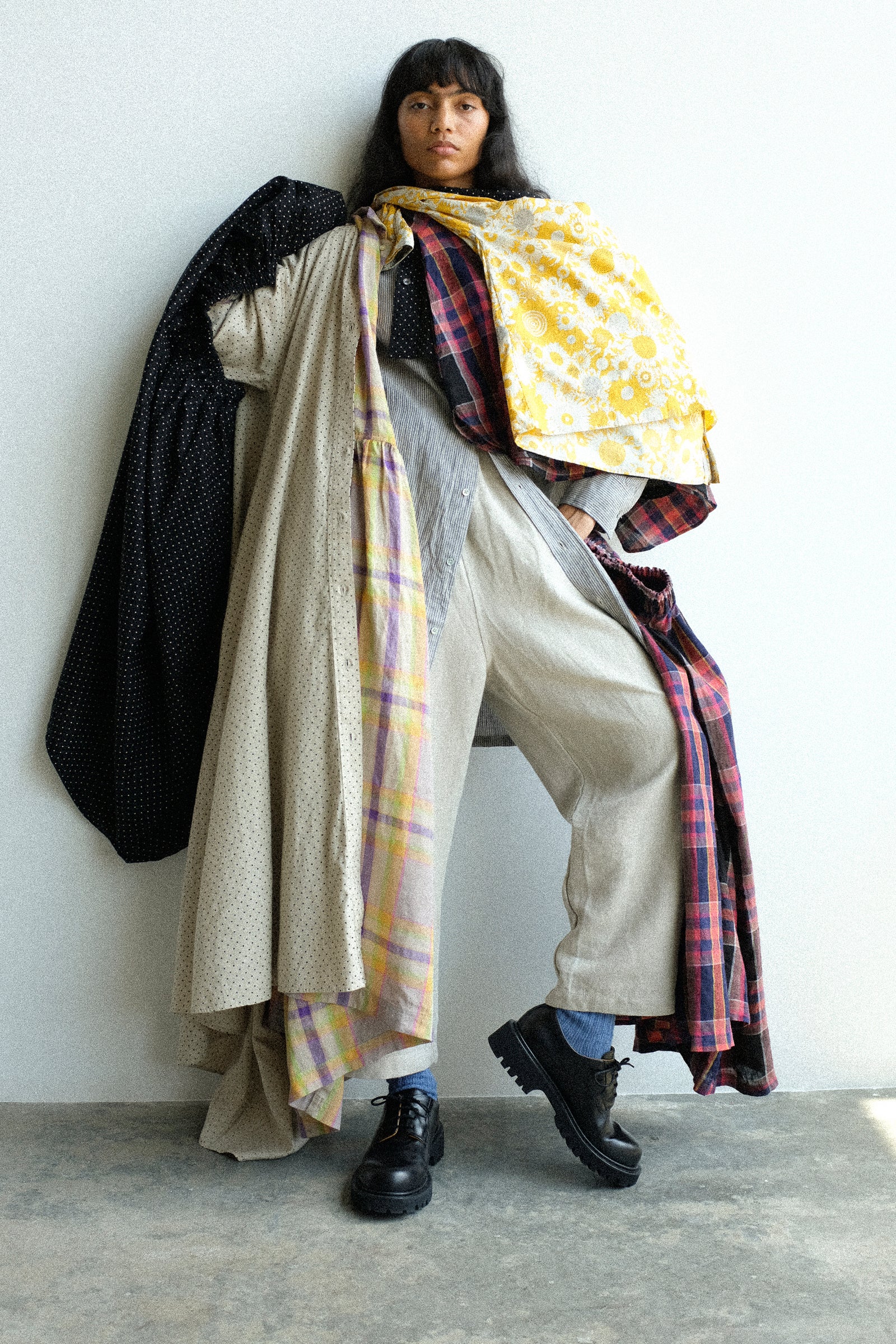 A woman with layers of Ichi Antiquites clothing, leaning against a white wall.