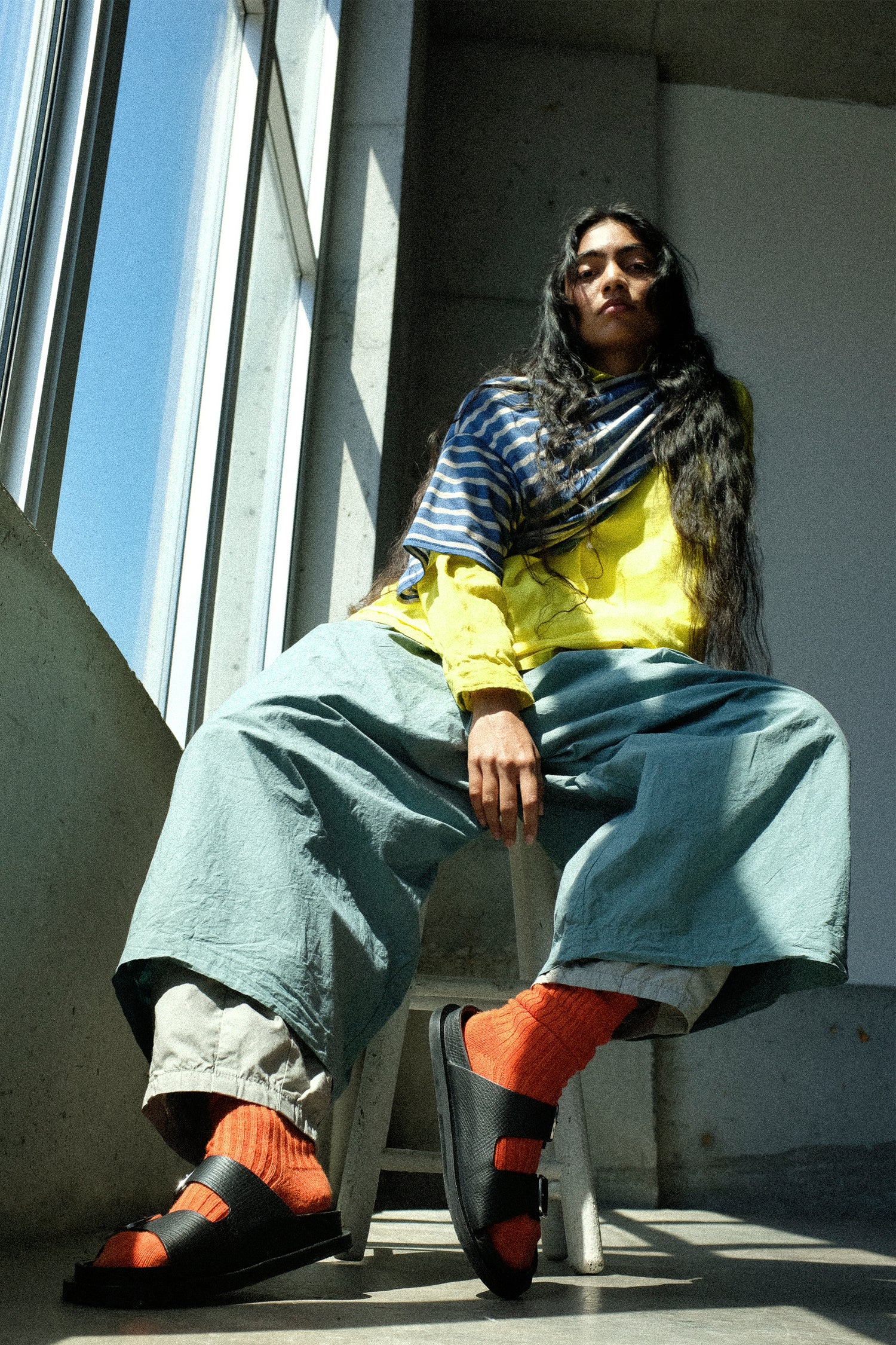 Person sitting on a ledge wearing a striped shirt, yellow jacket, and colorful shoes.