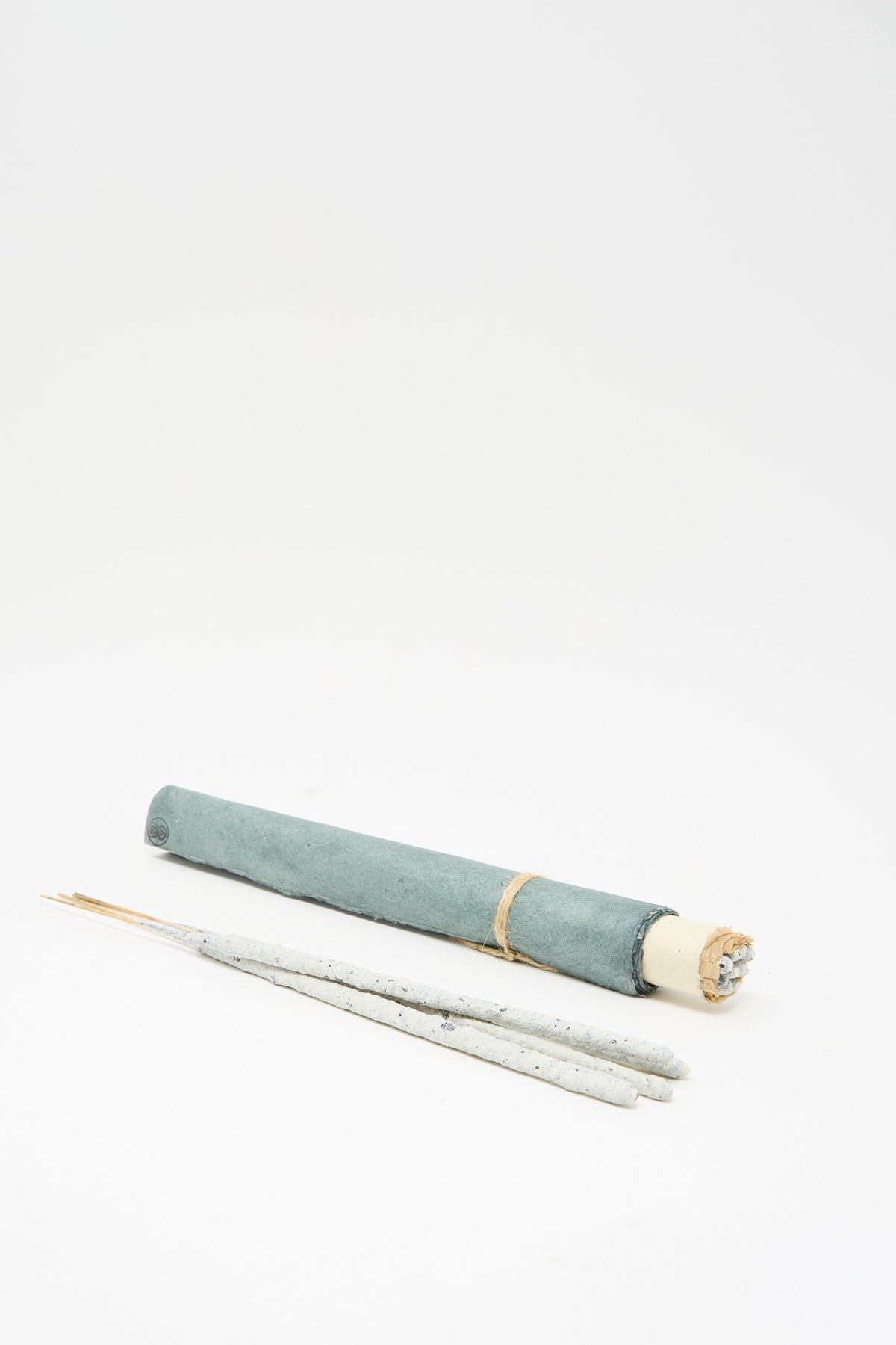An Incausa Copal Incense Scroll, featuring a rolled, sage-colored paper holder tied with twine and three pale, handmade-in-Mexico incense sticks lying in front.