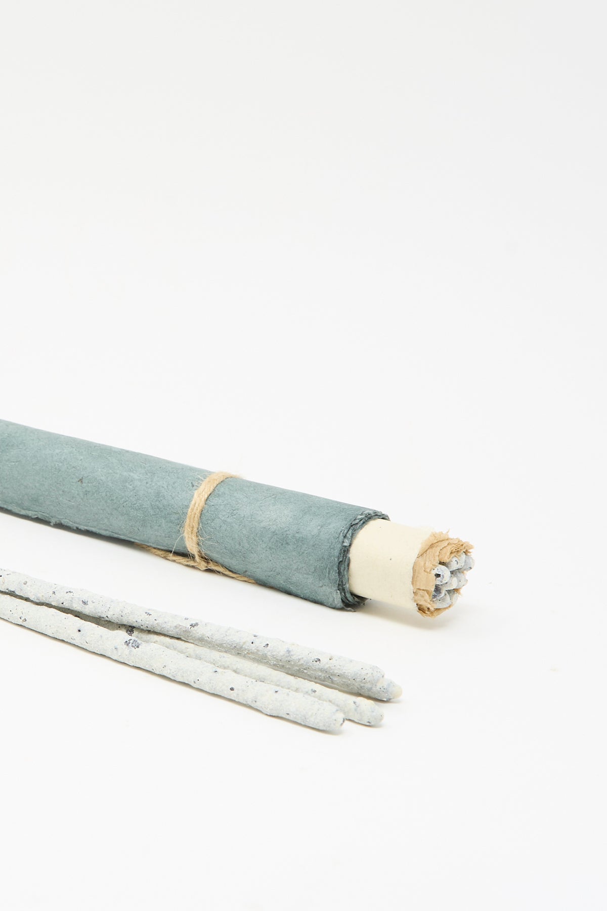A bundle of Incausa Copal Incense Scroll sticks wrapped in blue-grey paper secured with twine, with three loose sticks lying in the foreground.