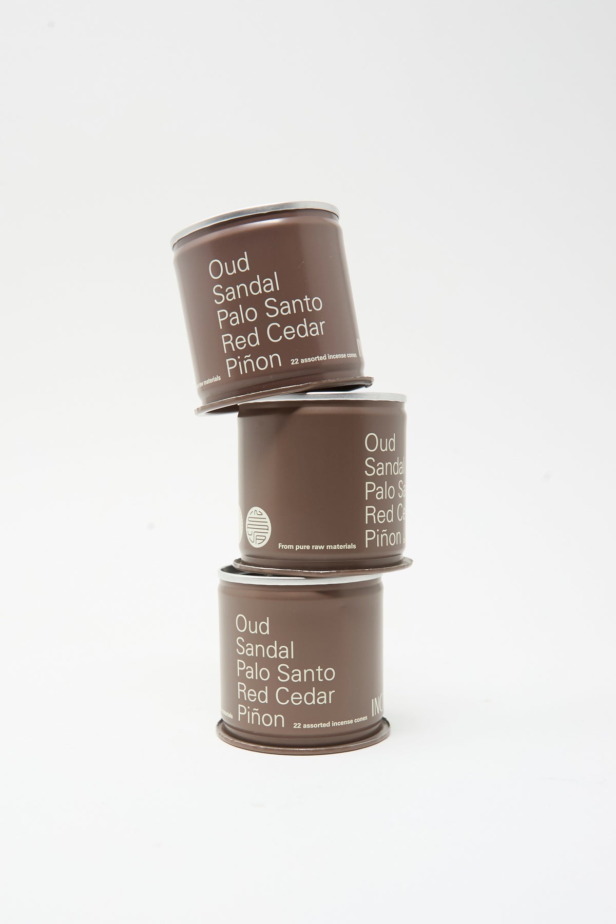 Three brown cylindrical tins of Incausa Discovery Incense Cones stacked vertically, each labeled with wood scents including Oud, Sandal, Palo Santo, Red Cedar, and Piñon.