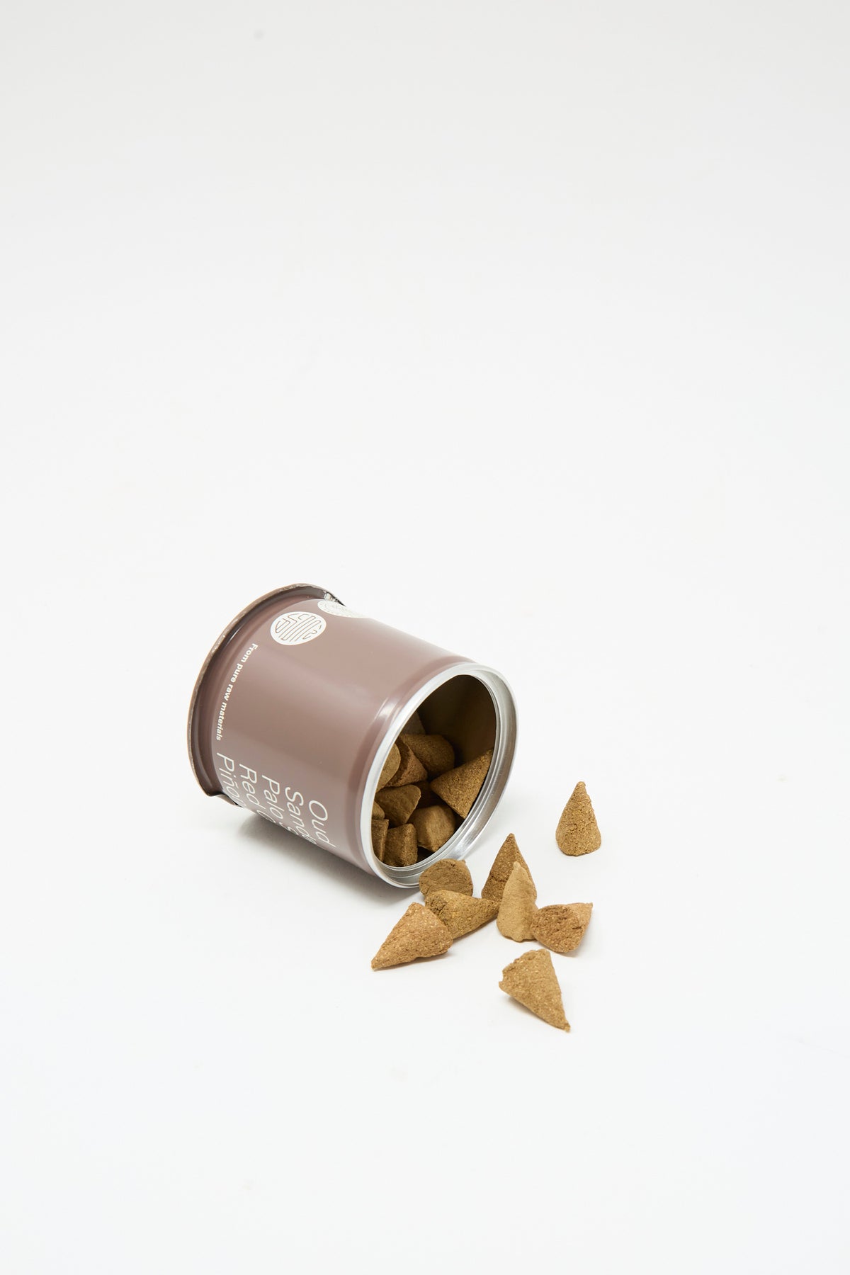 A brown cylindrical tin of Incausa Discovery Incense Cones tipped on its side, spilling several tan incense cones onto a white surface.