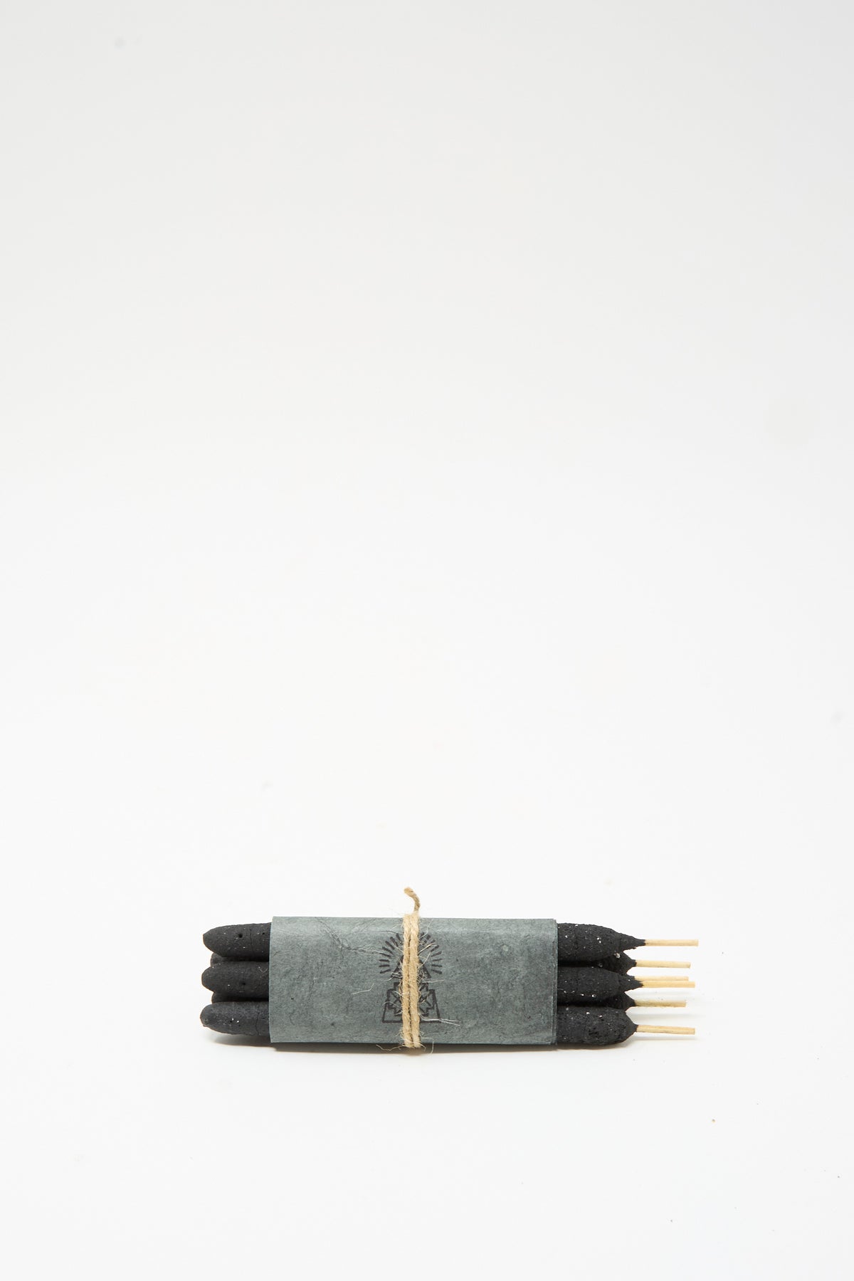 A bundle of six black Half Dozen Incense Bundles in White Sage resin sticks wrapped in gray paper and tied with twine.
