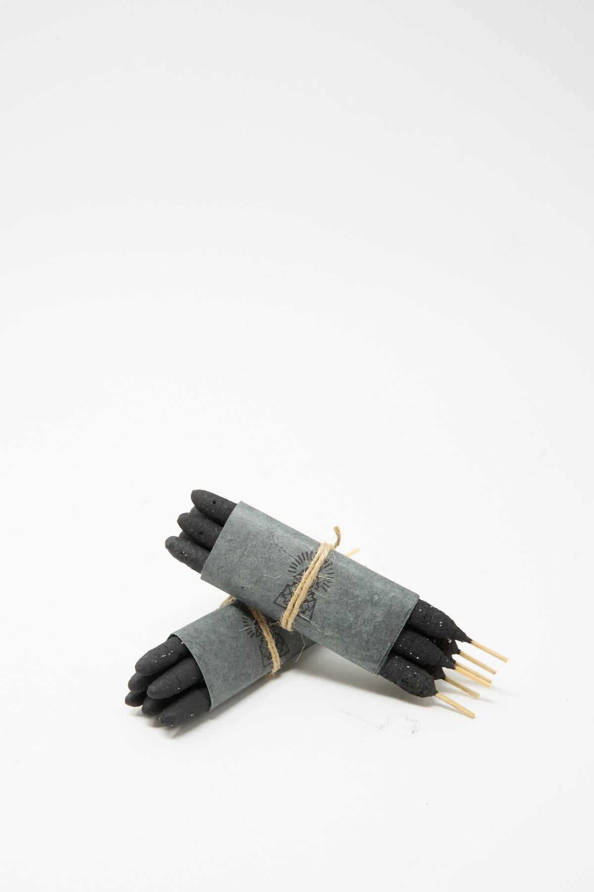 Two bundles of Half Dozen Incense Bundles in White Sage, presented as black artisanal incense sticks wrapped in grey paper and tied with twine.