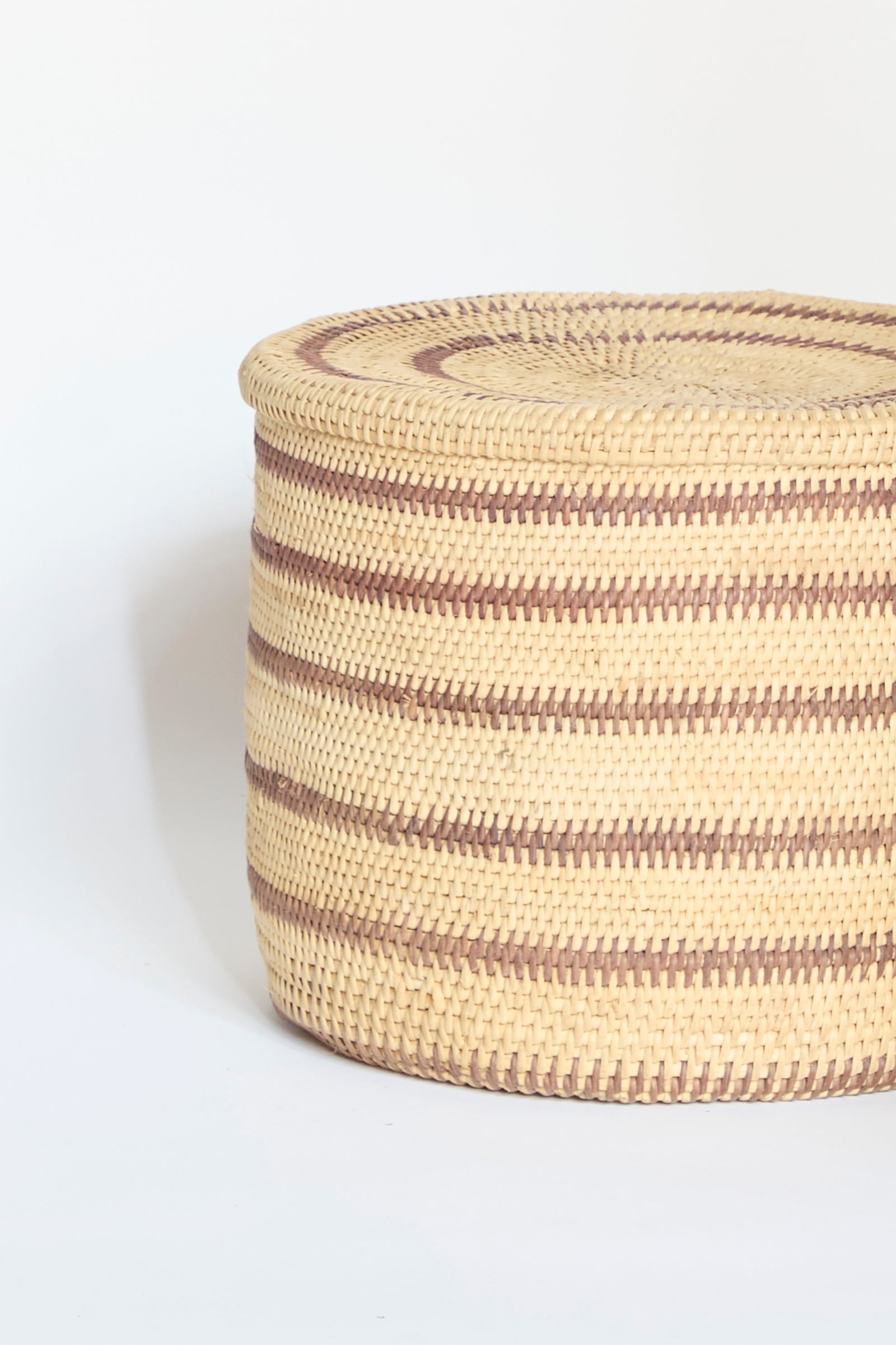 The Motorohina Basket with Yanomami Stripe Painting by Incausa, featuring alternating light and dark horizontal stripes, sits on a plain white background.
