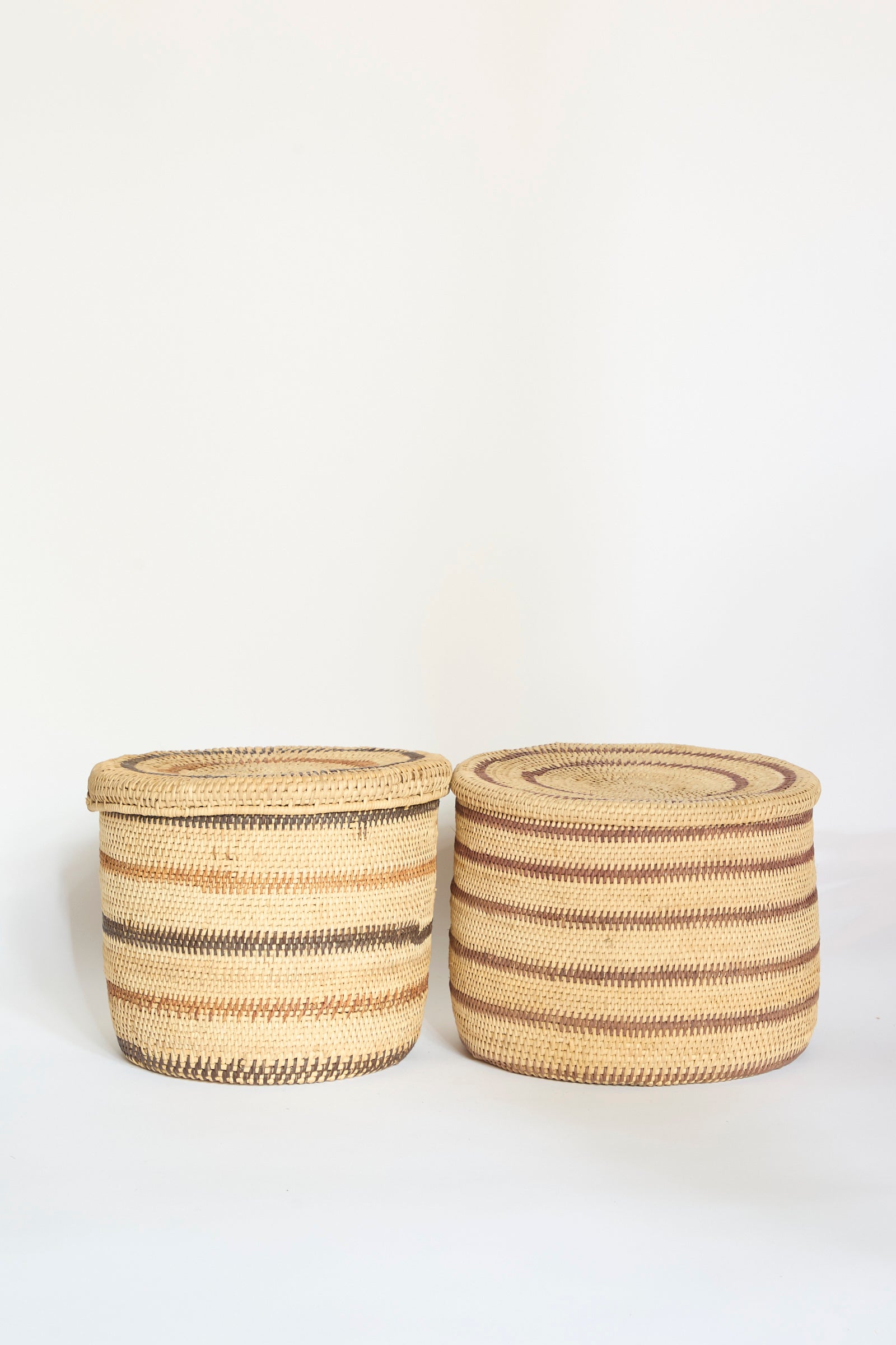 Two round Motorohina Baskets with Yanomami Stripe Painting Mixed from Incausa—each a beautiful handwoven Amazon basket—feature brown, tan, and beige horizontal stripes, sitting side by side against a plain white background.