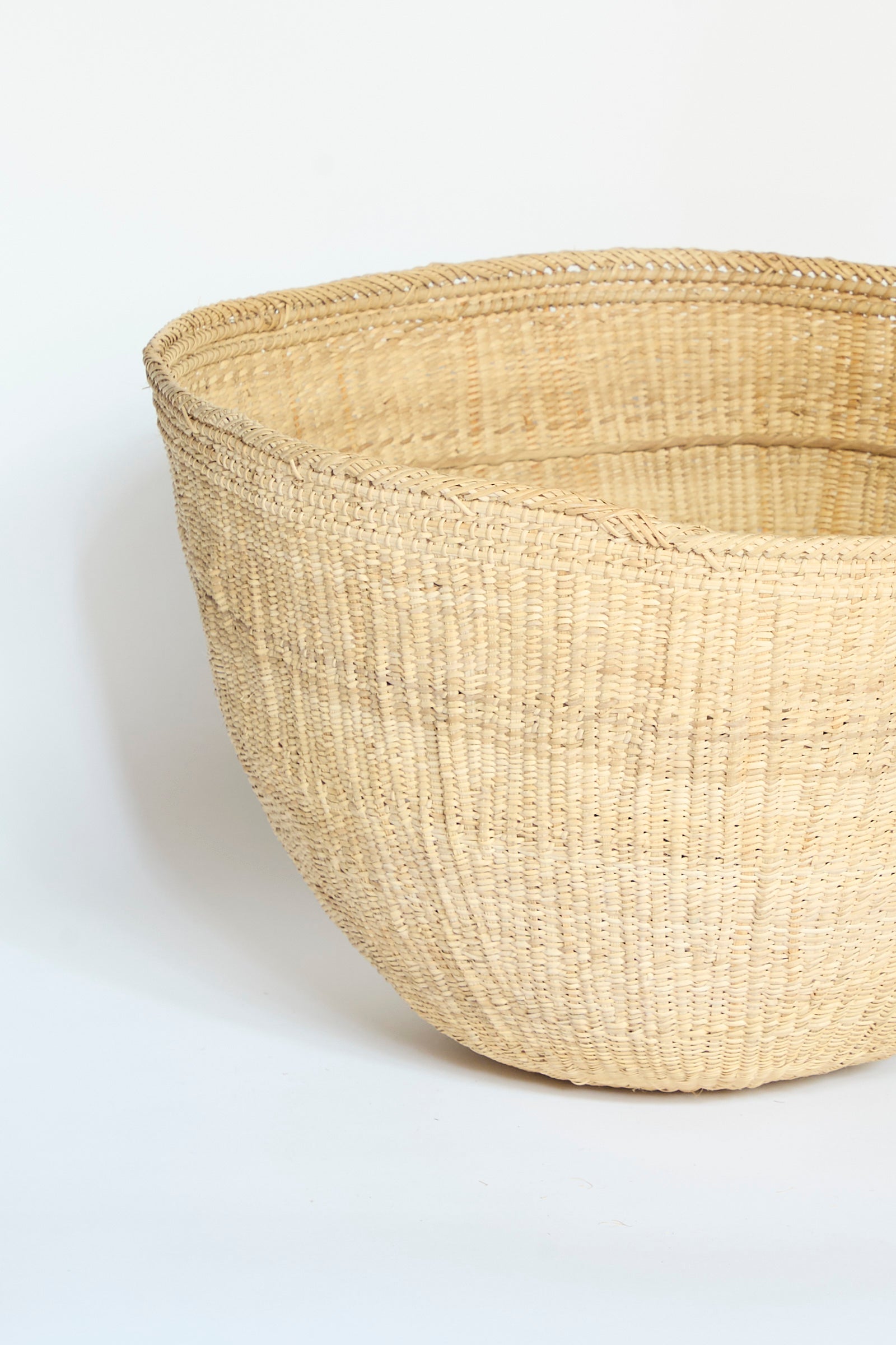 The Yanomami Wii Basket Large in Natural by Incausa, a spacious round basket crafted from natural straw and inspired by traditional Yanomami storage baskets, is displayed against a plain white background.