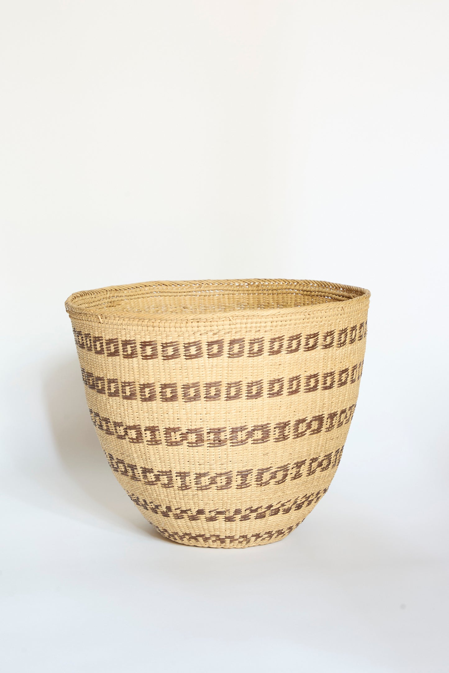 The Yanomami Wii Basket Large in Natural with Squares by Incausa is a handwoven storage basket crafted from Titica vine, featuring geometric brown square patterns arranged in horizontal rows on a light tan background, inspired by traditional Yanomami designs from the Amazon and displayed against a plain white surface.