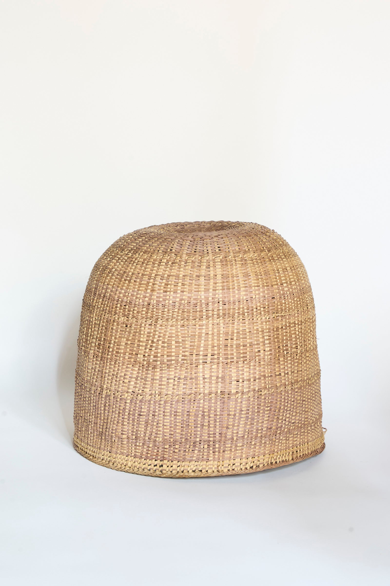 A large, dome-shaped Yanomami Wii Basket XL in Mixed Pigment by Incausa, handwoven from natural Titica vine and showcasing a light brown hue, sits on a plain white surface.