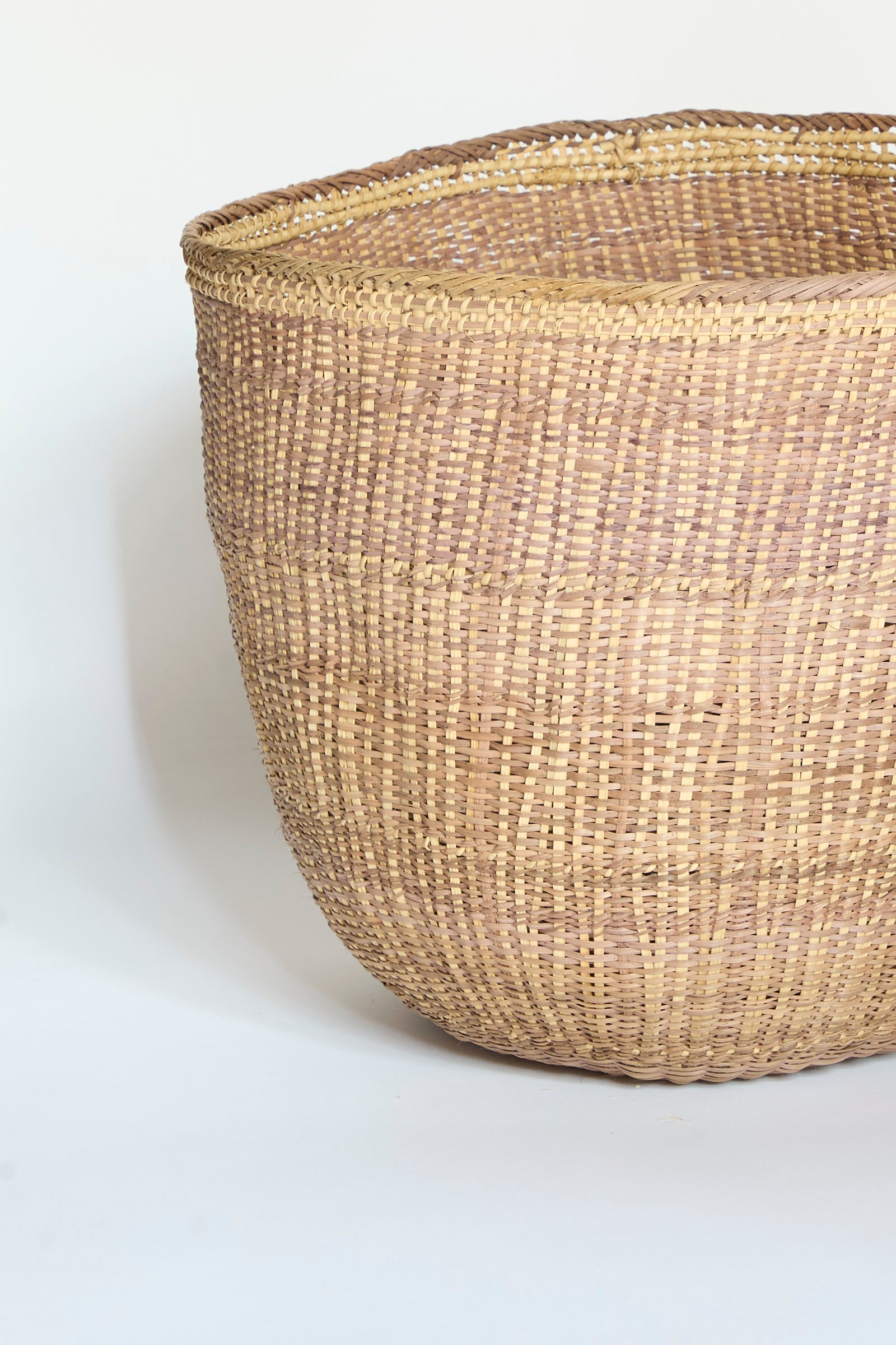 The Yanomami Wii Basket XL in Mixed Pigment by Incausa, a large handwoven basket crafted from natural Titica vine, rests on a neutral background, showcasing its textured surface and distinctive upper rim.