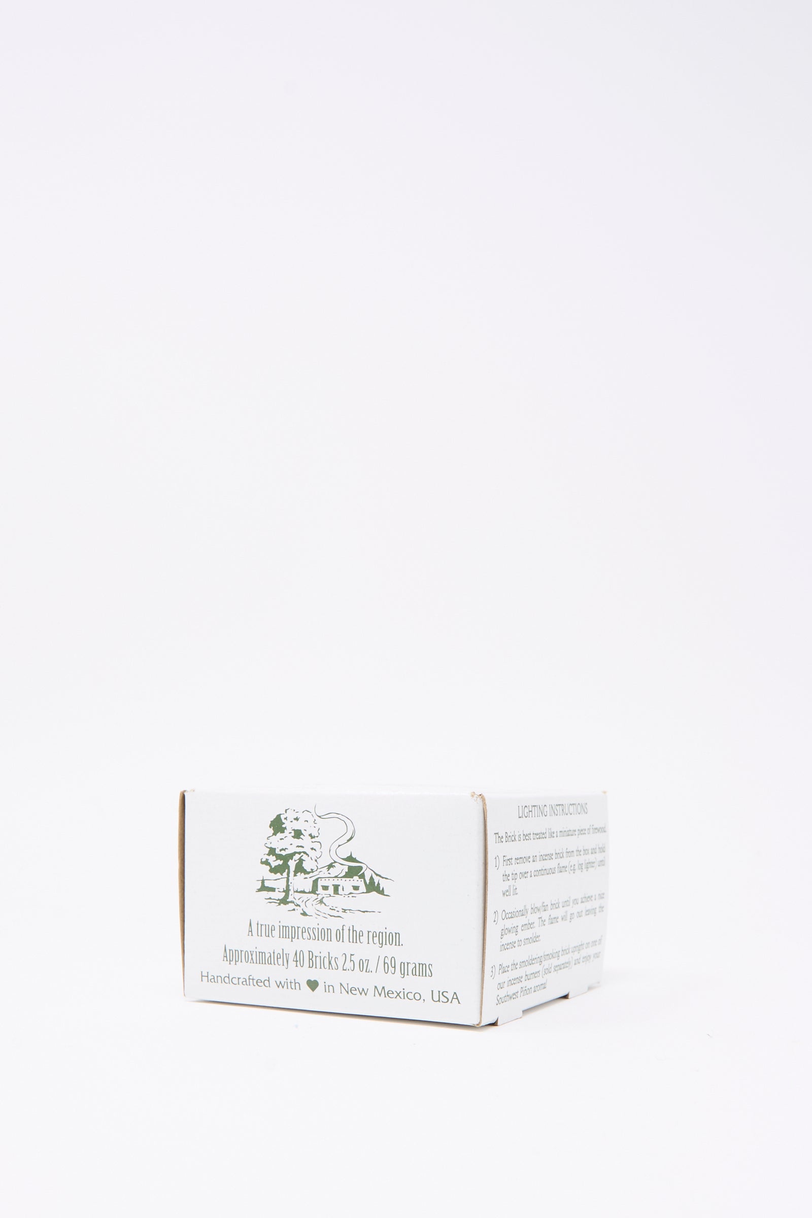 The Piñon Incense Box by Incense of the West features a small white box with green text and illustration, handcrafted in New Mexico—ideal for storing piñon pine incense or using with New Mexican clay burners.