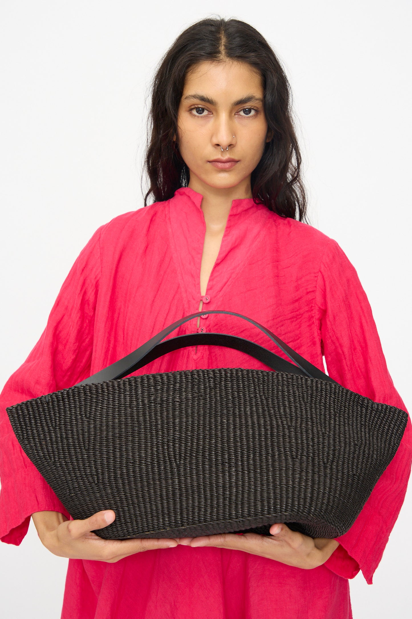 A person holds the Inès Bressand Large Gousse Bag in Black with two handles against a plain white background.