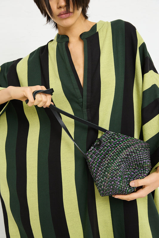 Woman in a striped dress holding an Inès Bressand N. 14 Mini Shell Bag in Green.