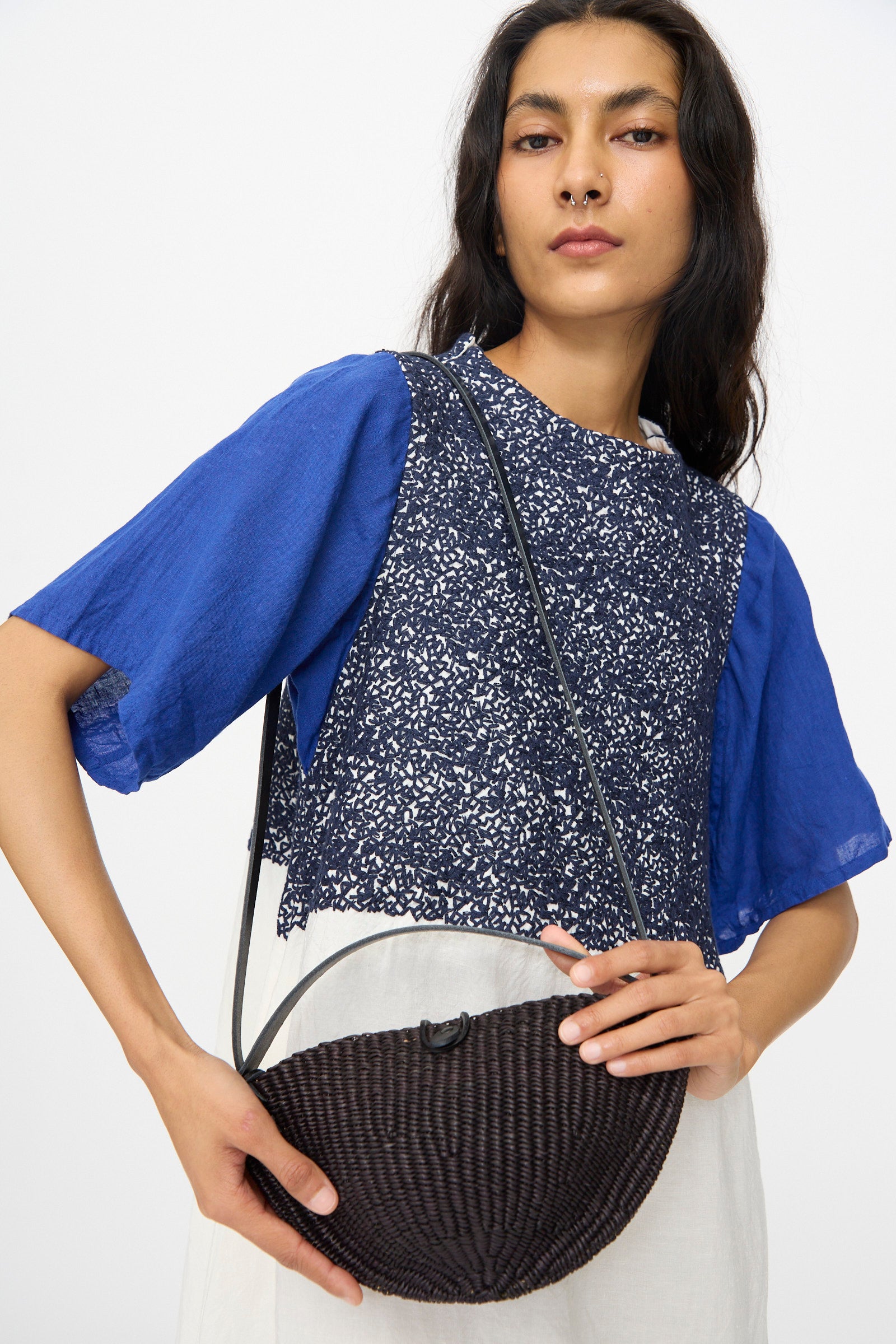 Person with long dark hair wears a blue and white patterned top, holding the Inès Bressand Small Walnut Bag in Black, standing against a plain background.