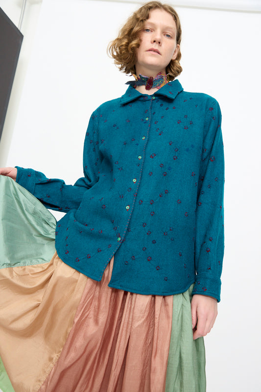 A person wearing the Injiri Bandhani Wool Shirt in Blue, a handcrafted piece from India, styled with a long color-blocked skirt in green and peach tones, standing against a plain white background.