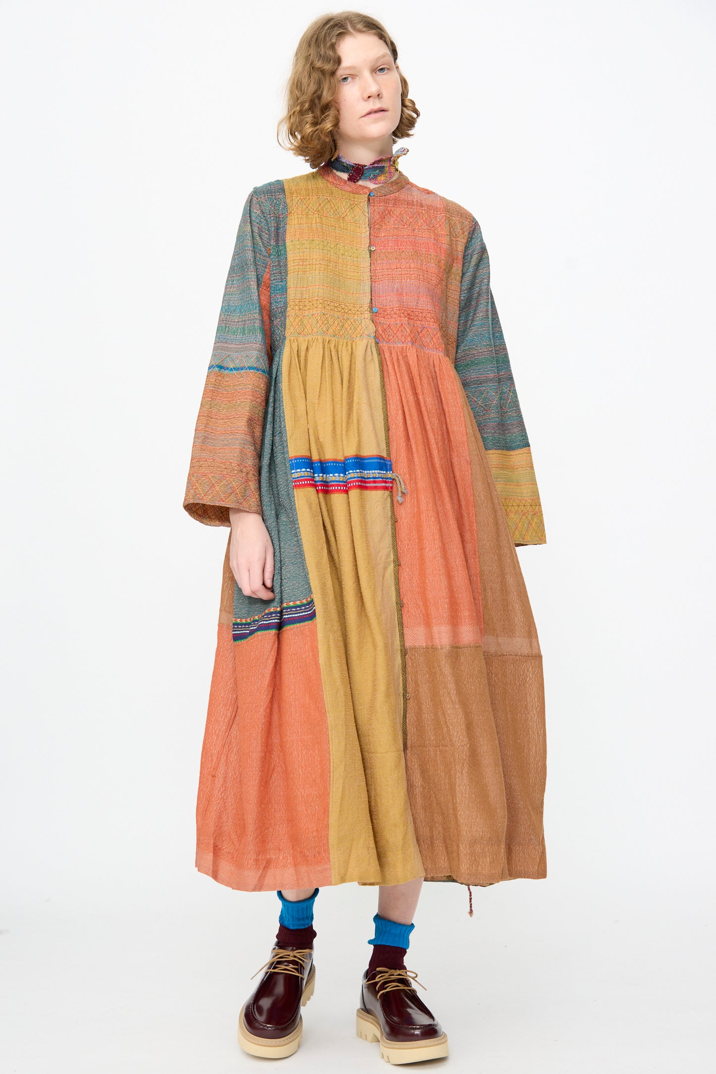 A person wearing the Injiri Bhujodi Wool and Silk Boro Jacket in Multi, styled with blue socks and platform shoes, stands against a plain white background.
