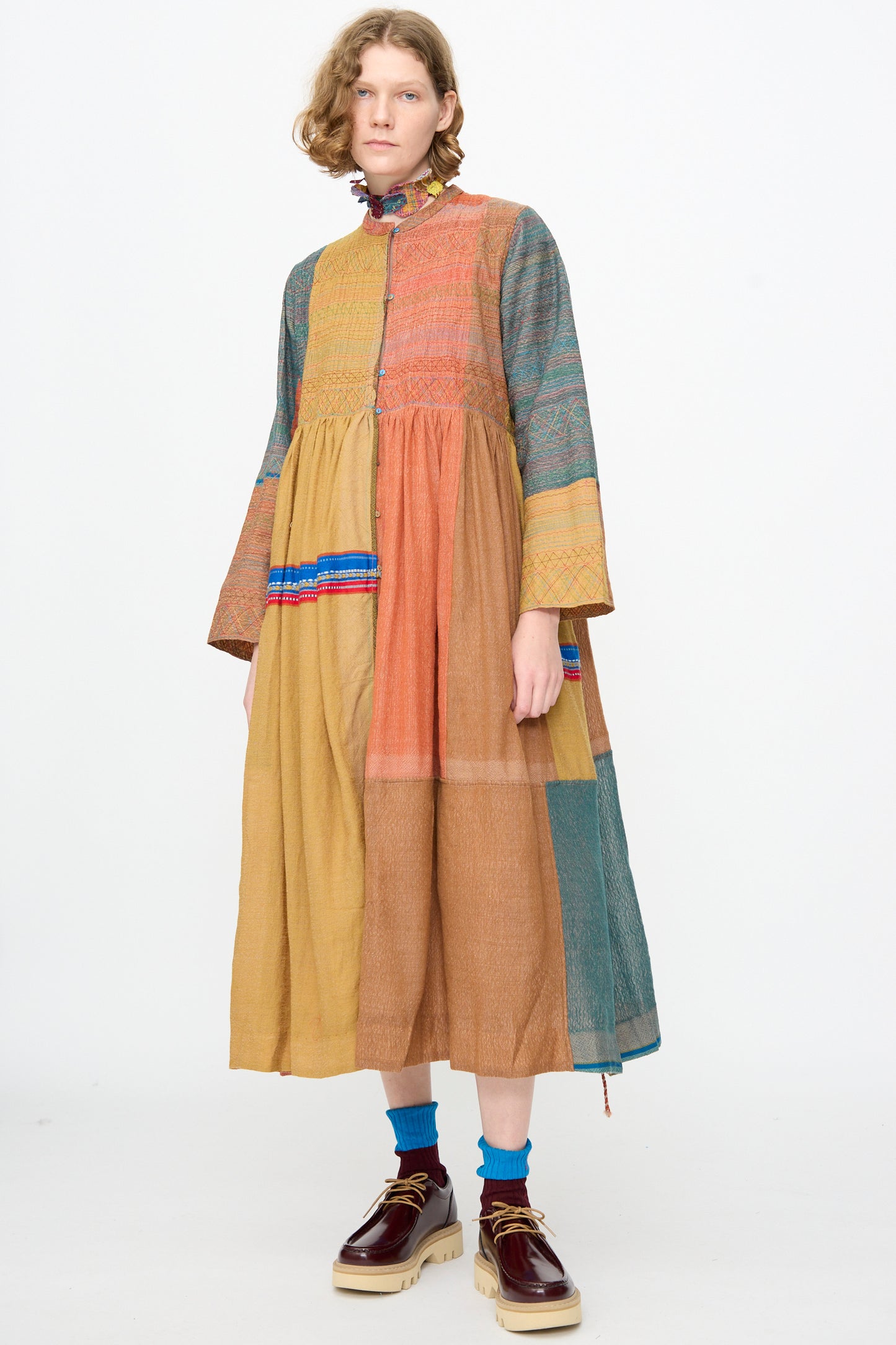 A person wearing the Injiri Bhujodi Wool and Silk Boro Jacket in Multi, styled with blue socks and brown platform shoes, stands against a plain white background.