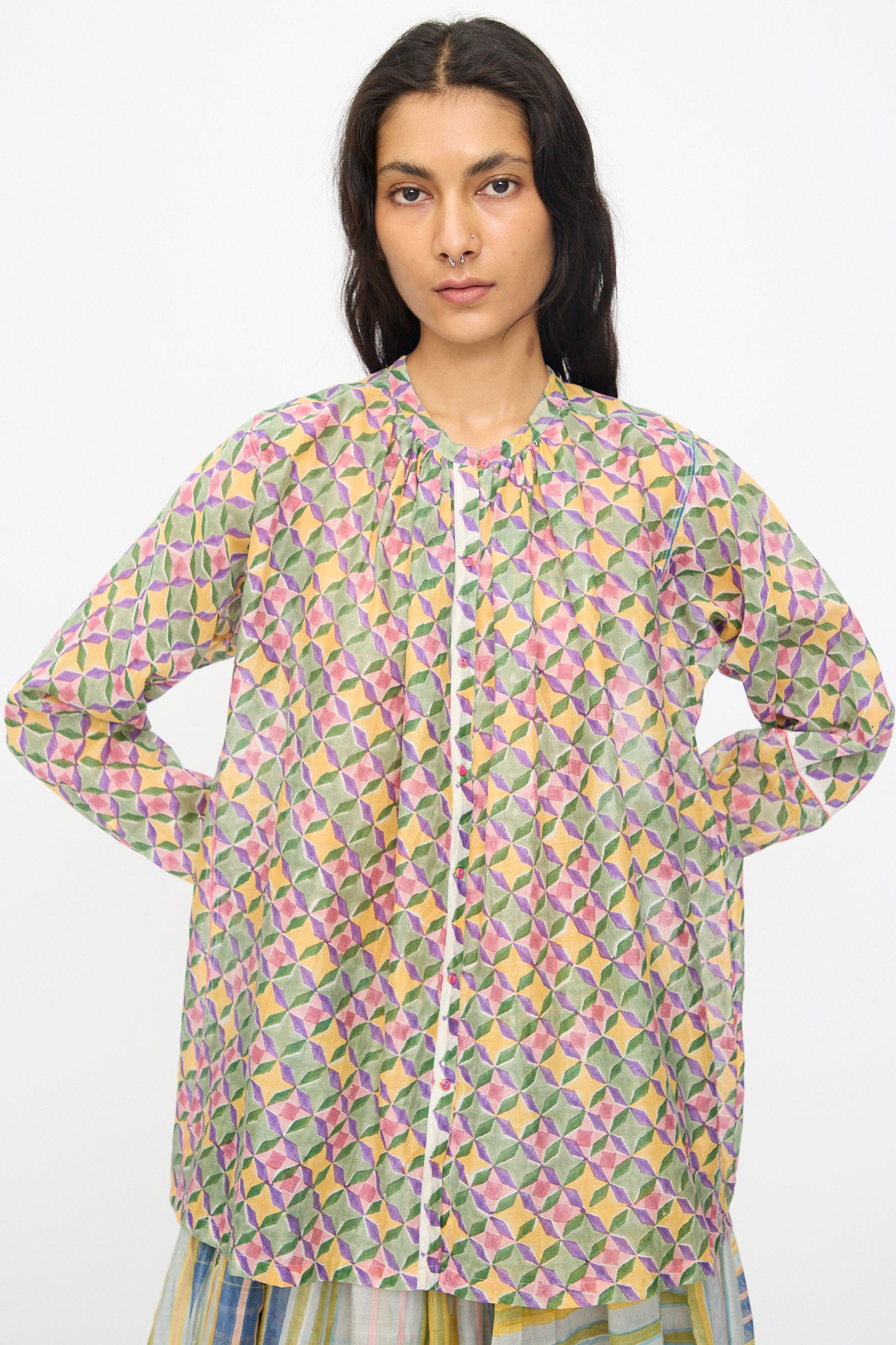 A person models the Injiri Blockprint Chanderi Oliver Shirt in Multi, featuring vibrant geometric patterns and long sleeves, standing with hands on hips against a plain white background.