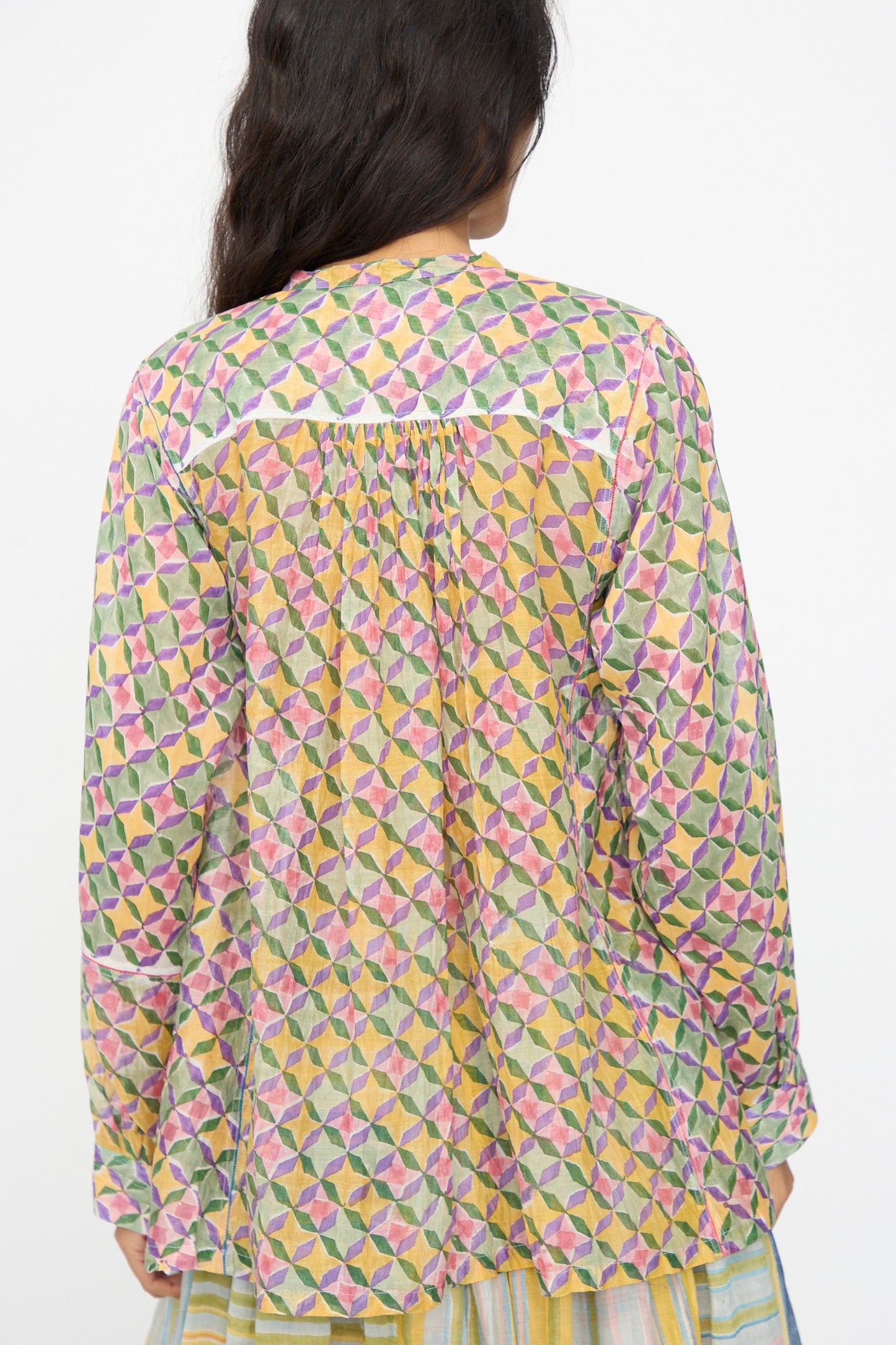 A person with long dark hair, seen from behind, wears the Injiri Blockprint Chanderi Oliver Shirt in Multi, featuring a loose fit and colorful geometric patterns.