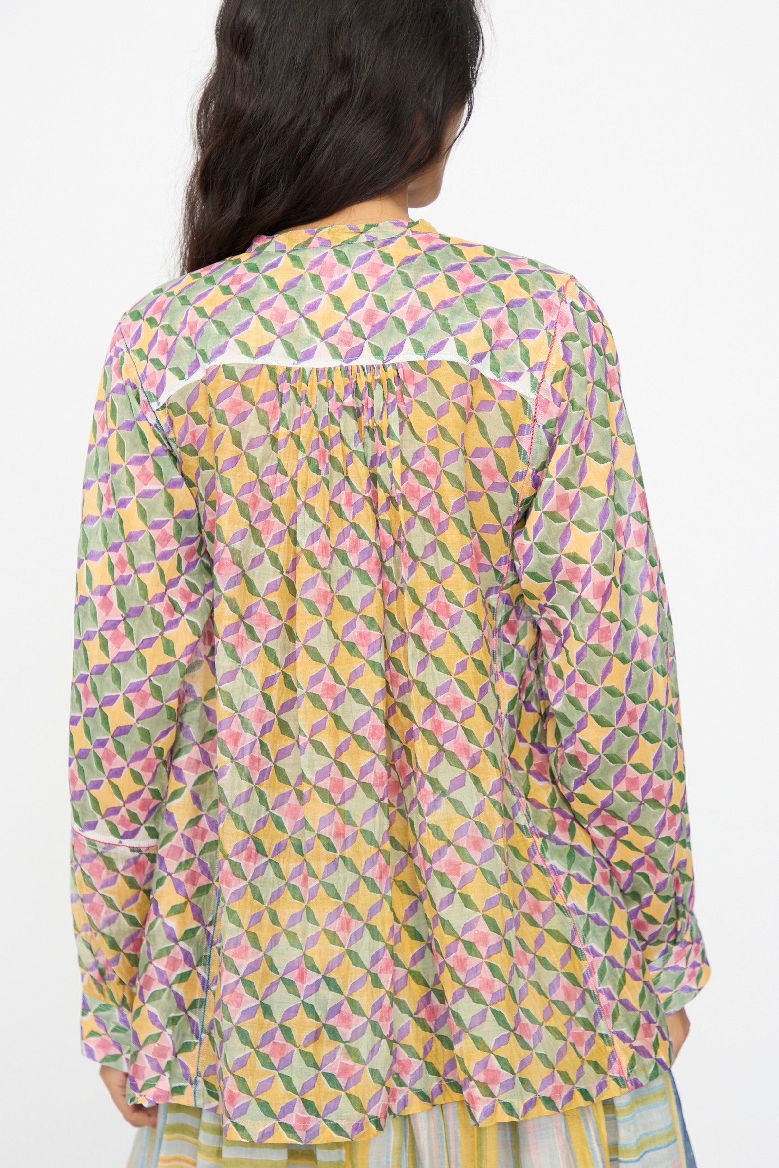 A person with long dark hair, seen from behind, wears the Injiri Blockprint Chanderi Oliver Shirt in Multi, featuring a loose fit and colorful geometric patterns.