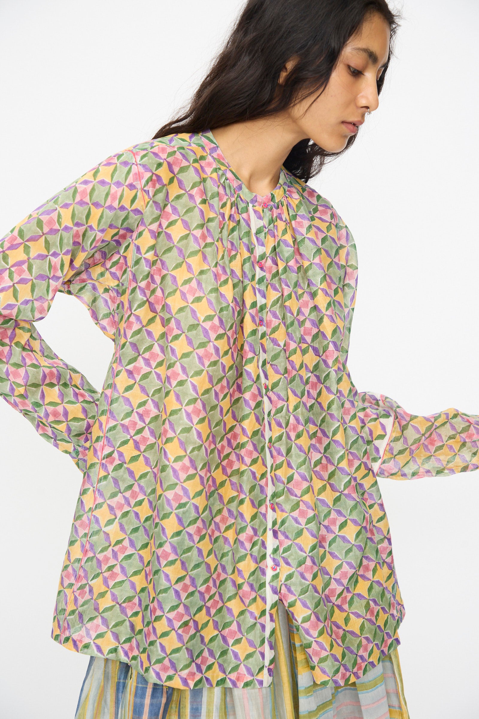 A person wears the Injiri Blockprint Chanderi Oliver Shirt in Multi, featuring a bold geometric pattern, paired with a striped skirt against a plain white background.