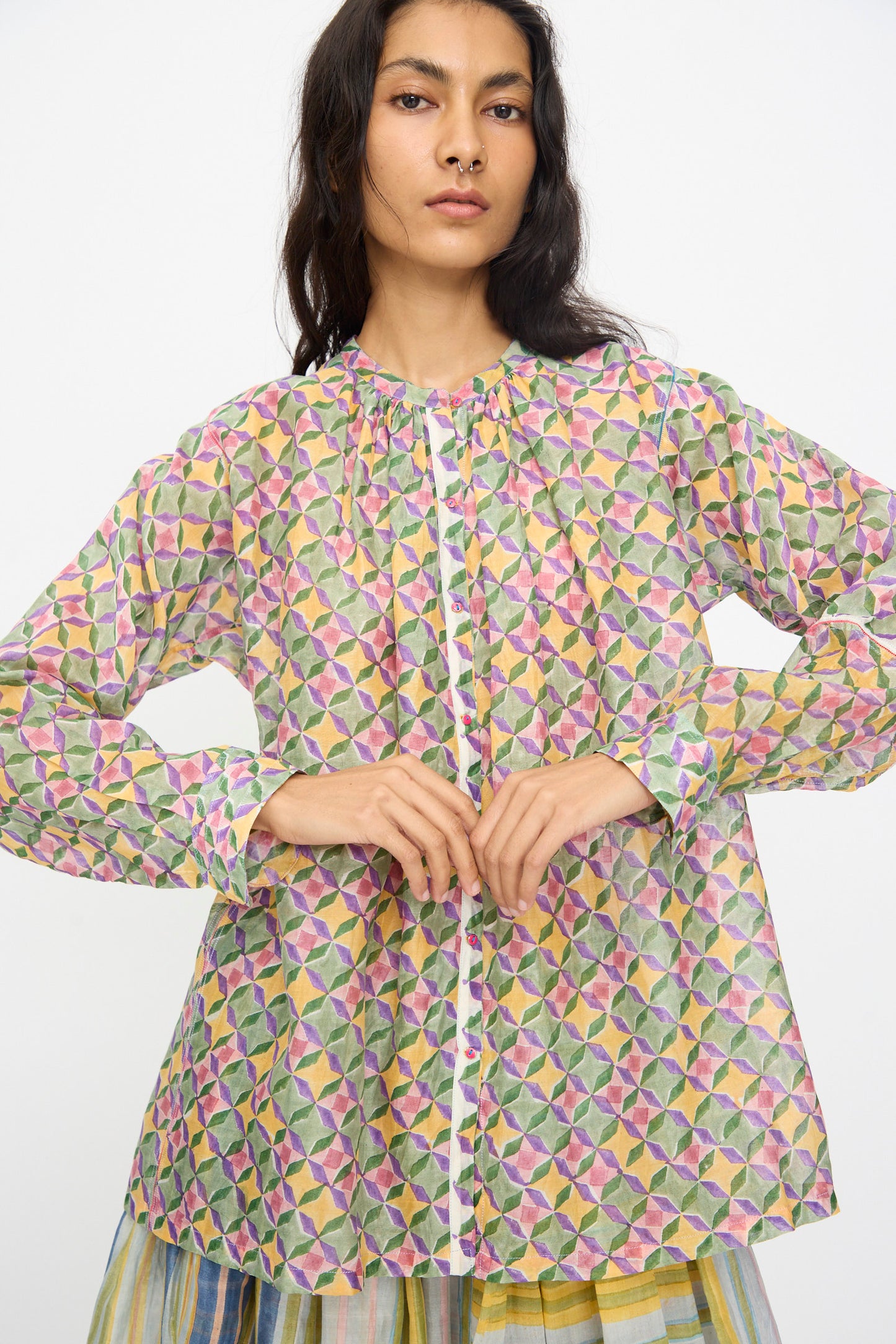 A woman wears the Injiri Blockprint Chanderi Oliver Shirt in Multi, featuring long sleeves and a colorful geometric pattern, standing against a plain white background.