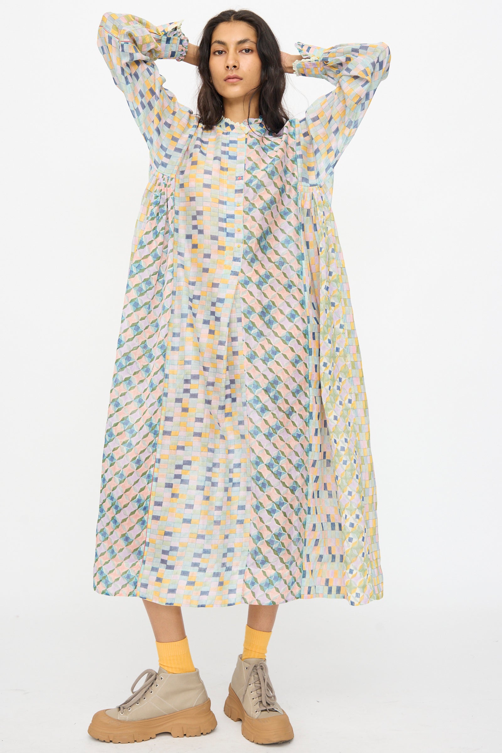 A person stands hands behind head in the Injiri Blockprint Chanderi Trumpet Dress in Blue Yellow Multi, paired with yellow socks and beige shoes, against a plain white background.