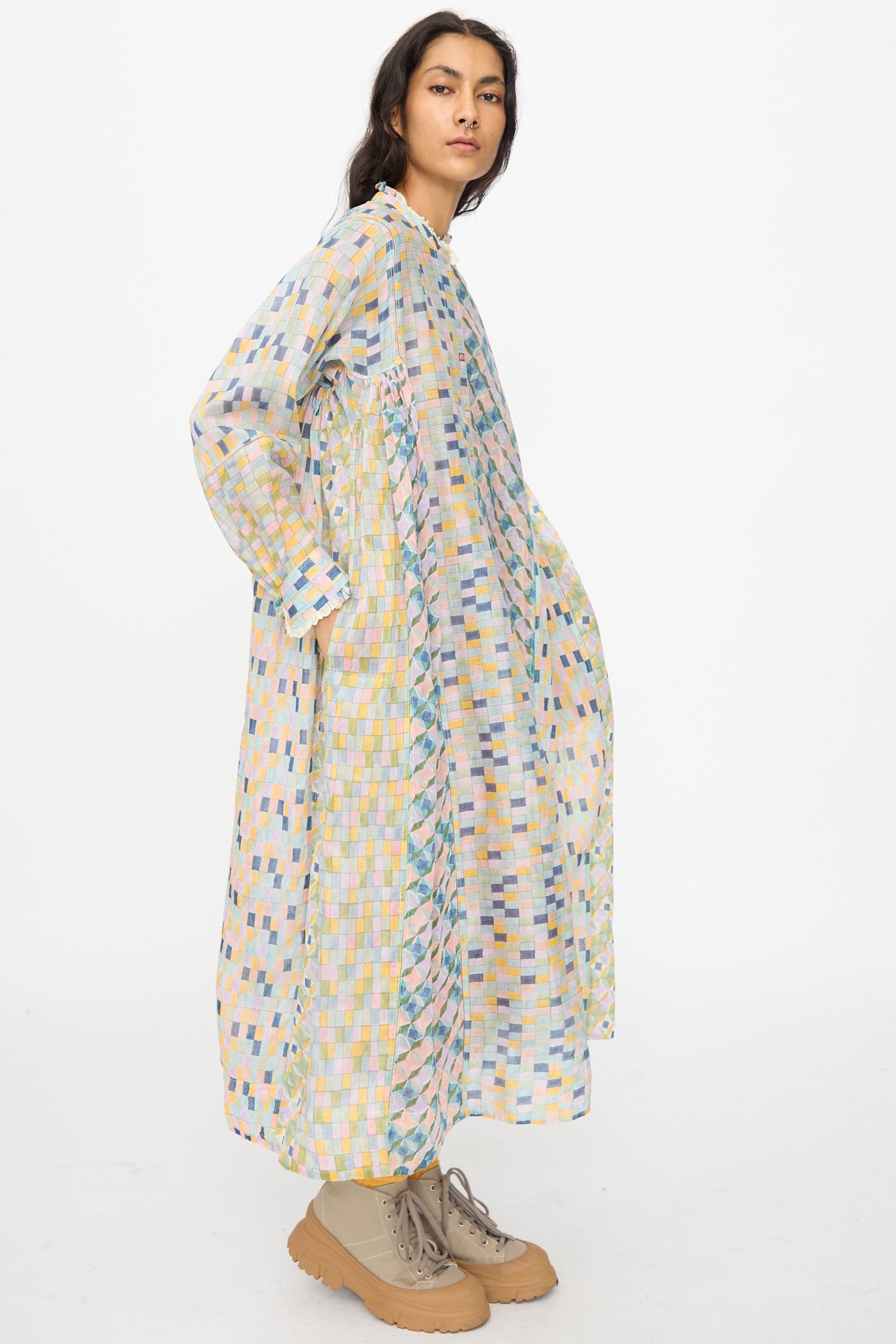 A woman stands sideways wearing the Injiri Blockprint Chanderi Trumpet Dress in Blue Yellow Multi with a colorful geometric pattern and tan lace-up shoes against a plain white background.