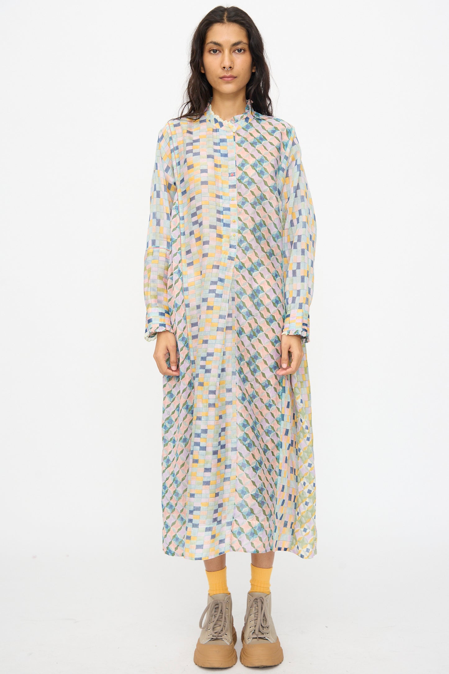A woman faces forward against a white background wearing the Injiri Blockprint Chanderi Trumpet Dress in Blue Yellow Multi with long sleeves, button-up front, yellow socks, and beige lace-up shoes.