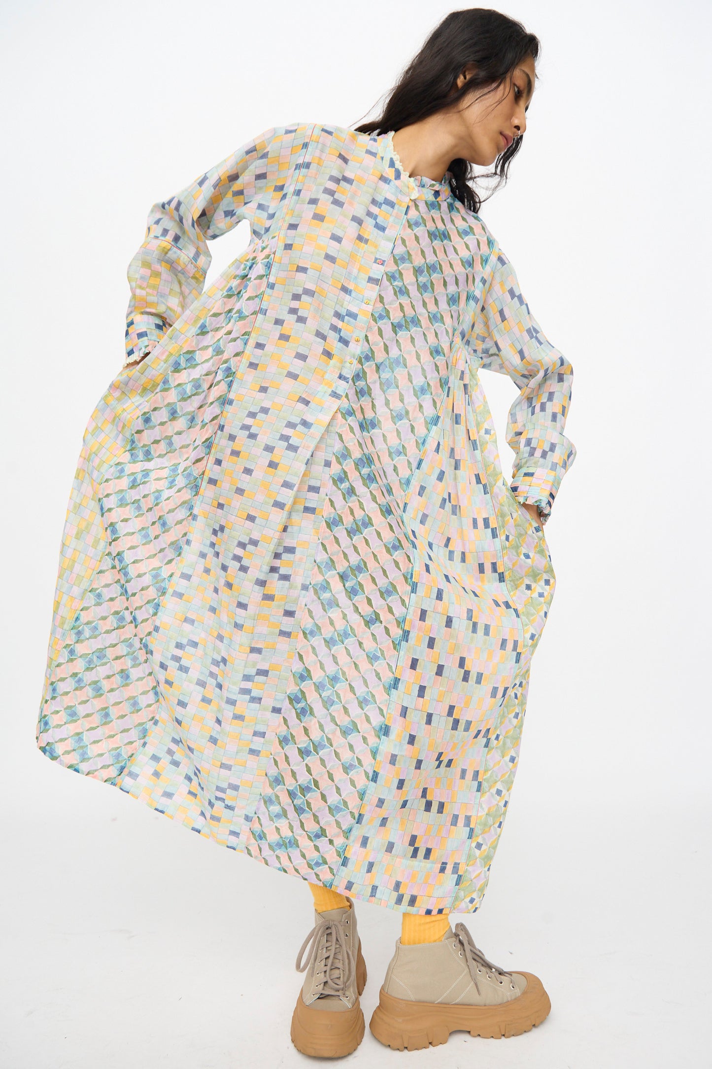 A woman models the Injiri Blockprint Chanderi Trumpet Dress in Blue Yellow Multi—loose, long-sleeved, and midi-length—paired with yellow socks and beige platform shoes, standing against a plain white background.