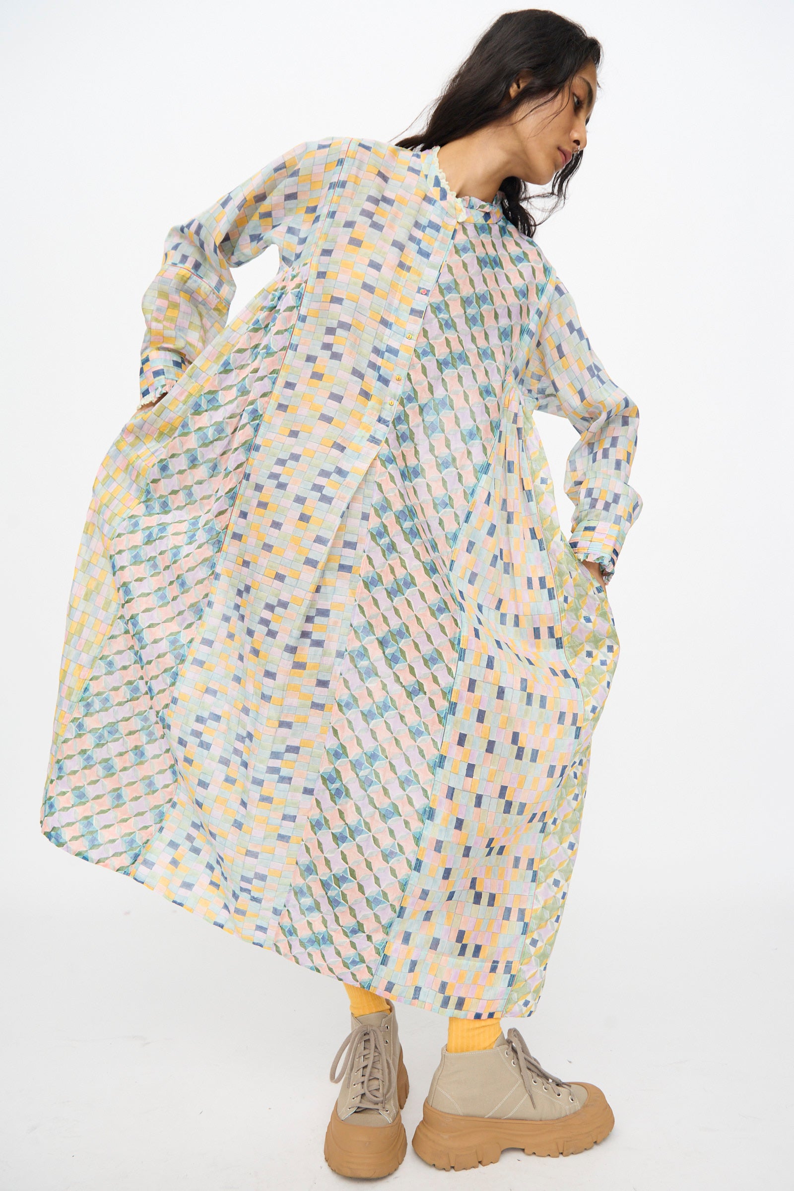 A woman models the Injiri Blockprint Chanderi Trumpet Dress in Blue Yellow Multi—loose, long-sleeved, and midi-length—paired with yellow socks and beige platform shoes, standing against a plain white background.
