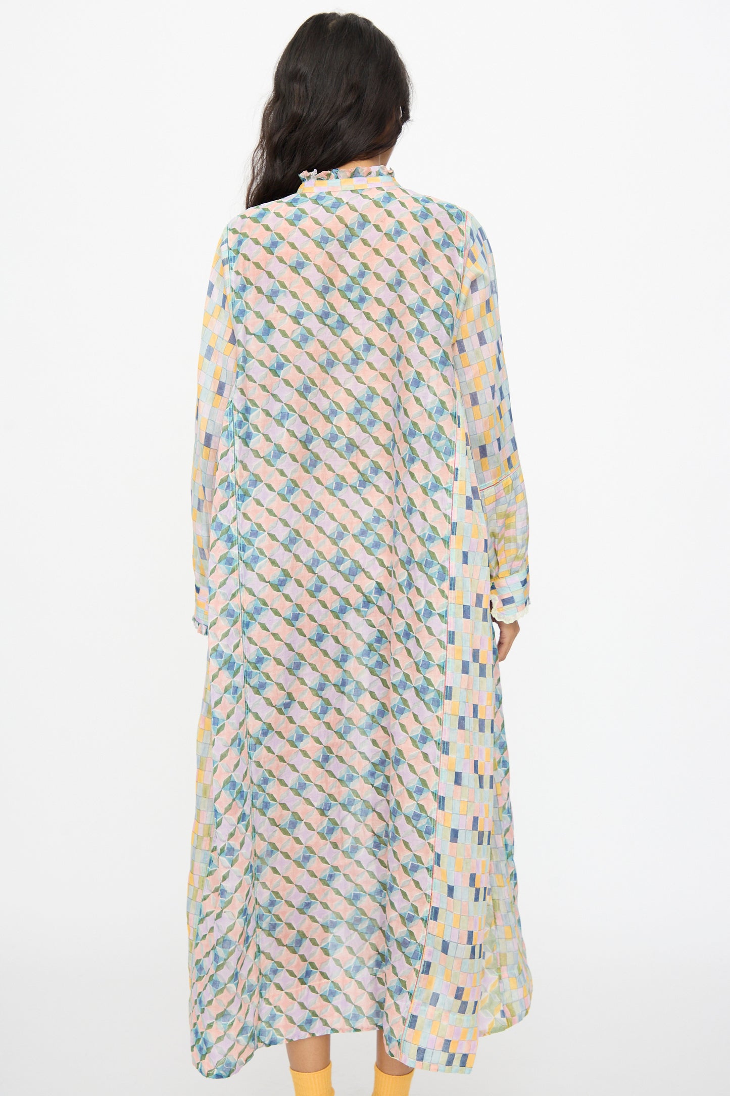 A person stands facing away, wearing the Injiri Blockprint Chanderi Trumpet Dress in Blue Yellow Multi, featuring a loose fit and colorful geometric block print. The background is plain white.