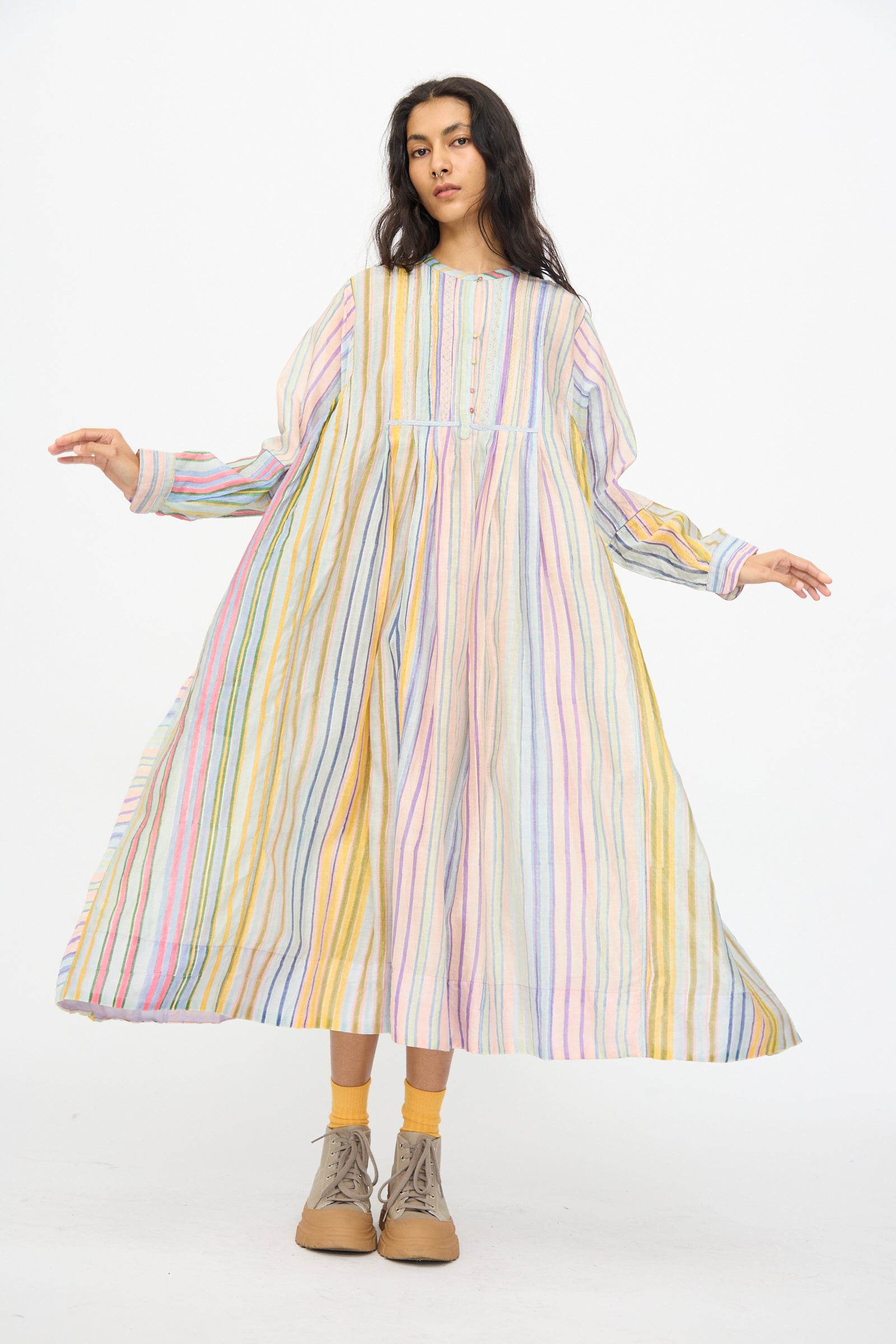 A woman wears the Injiri Blockprint Chanderi Trumpet Dress in Multi Stripe, paired with yellow socks and beige lace-up shoes, standing against a plain white background.
