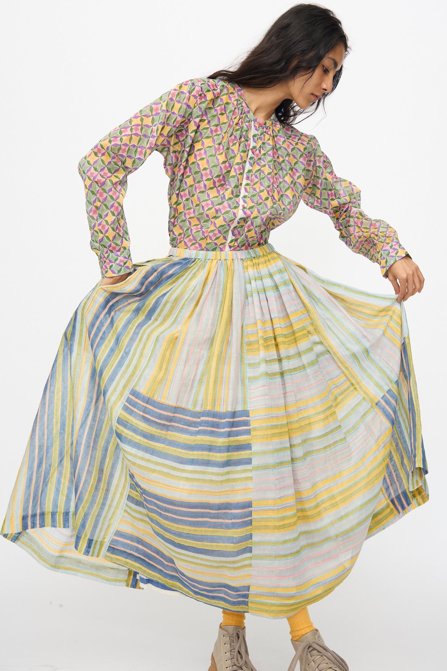 A woman models the Injiri Blockprint Chanderi Zamila Skirt in Green Multi, holding out its sides and looking down, against a plain white background.