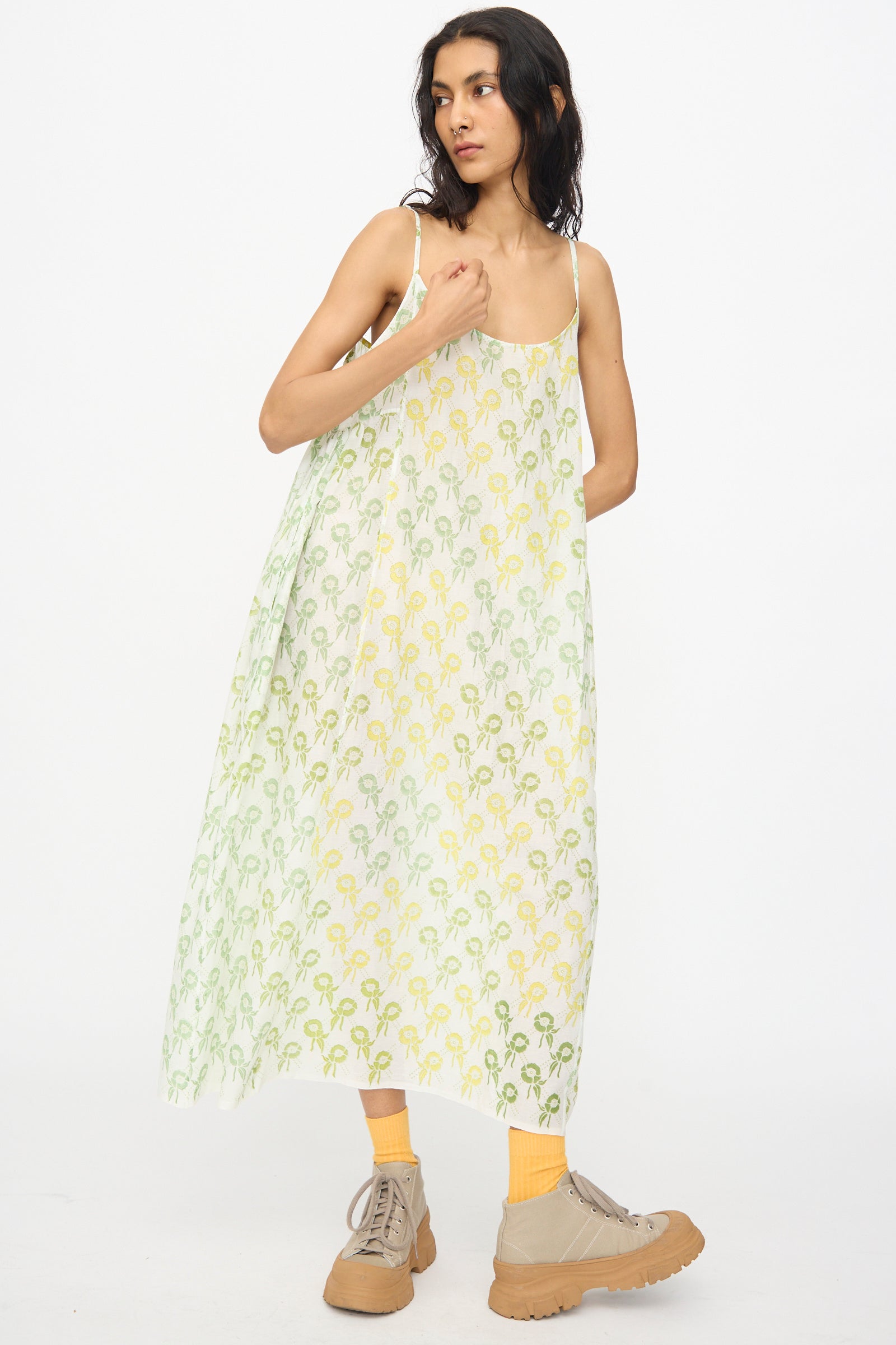 A person wears the Injiri Blockprint Cotton Emma Slip in Green Multi—a loose, sleeveless midi dress—paired with yellow socks and beige sneakers, standing against a white background.