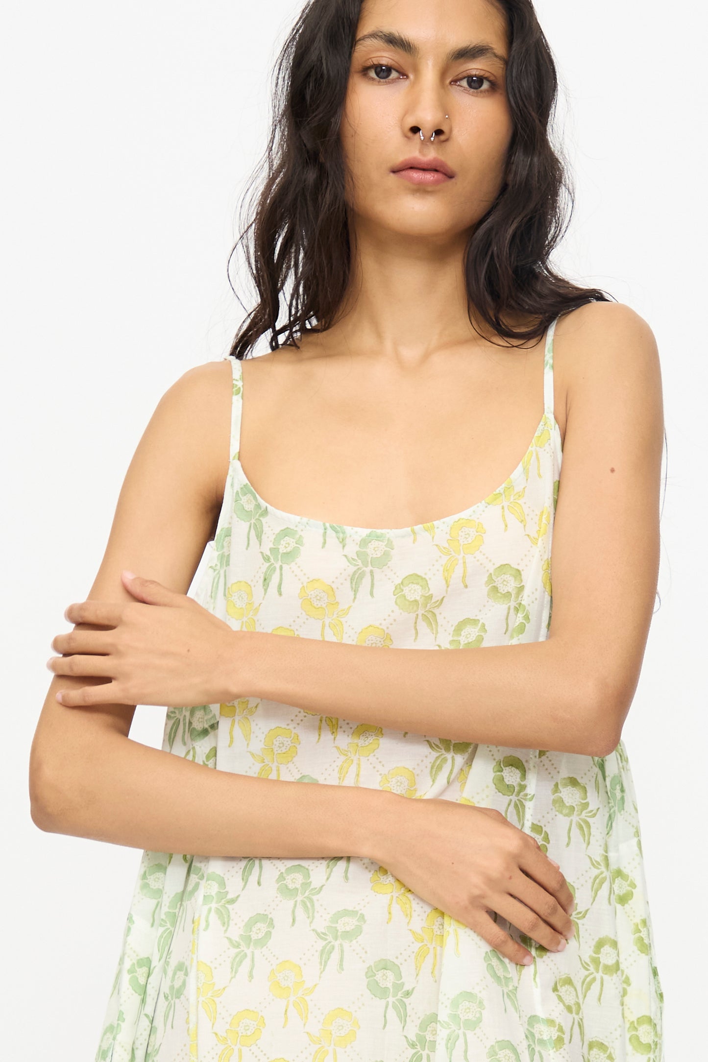 A woman with long dark hair wears the Injiri Blockprint Cotton Emma Slip in Green Multi, a sleeveless midi dress with thin straps, standing against a plain white background.