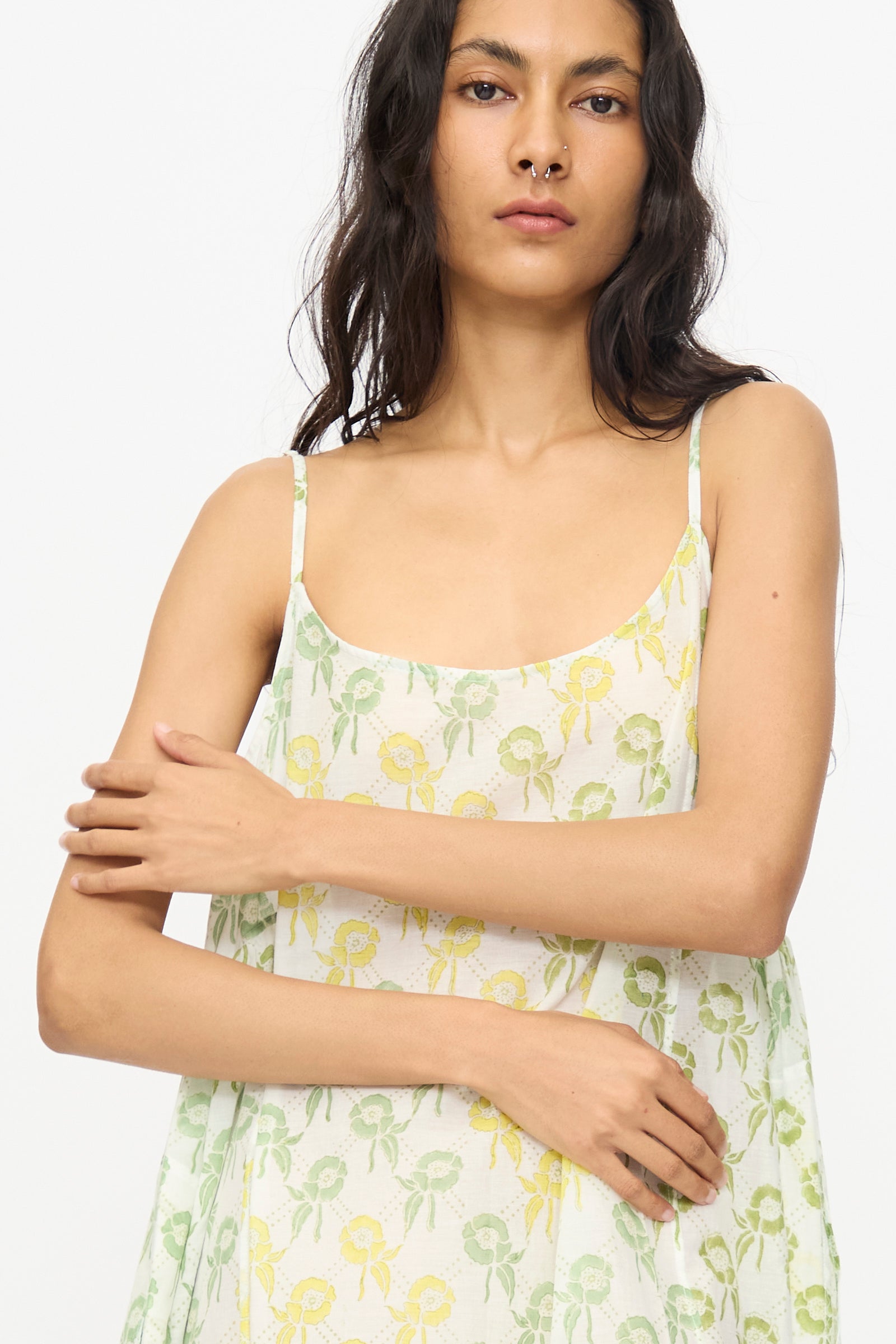 A woman with long dark hair wears the Injiri Blockprint Cotton Emma Slip in Green Multi, a sleeveless midi dress with thin straps, standing against a plain white background.