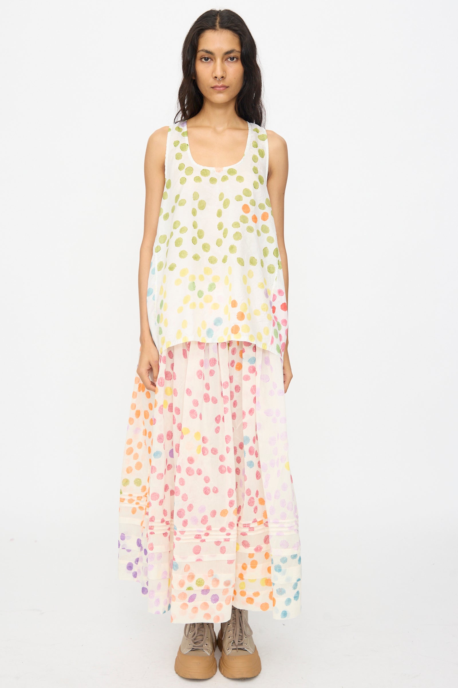 A woman faces forward wearing the Injiri Blockprint Silk Bandi Top in White Multi, a sleeveless, loose-fitting silk top with a colorful dotted design, paired with a long skirt and tan boots.