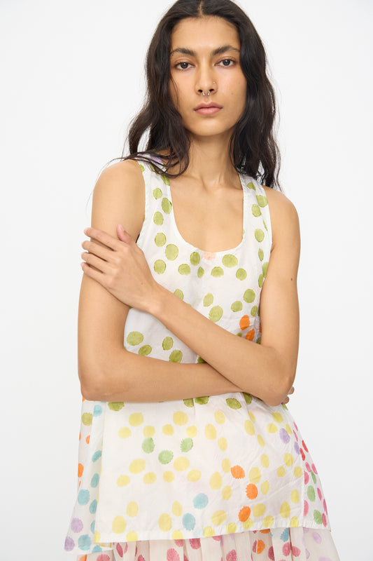 A woman with long dark hair stands against a plain background, wearing the Injiri Blockprint Silk Bandi Top in White Multi—a sleeveless silk top featuring a colorful dotted design.