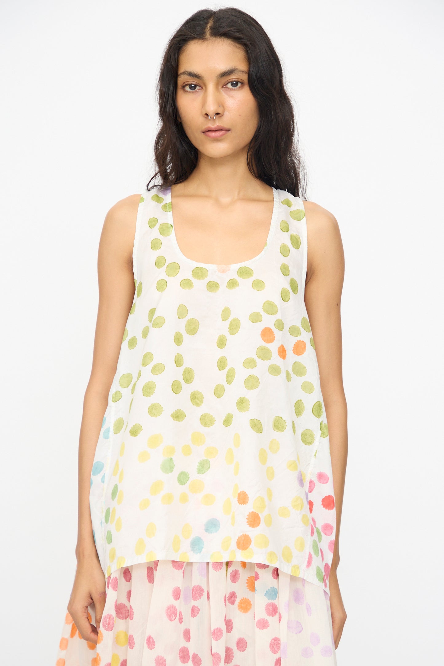 A woman faces forward wearing the Injiri Blockprint Silk Bandi Top in White Multi—a loose, sleeveless top with a colorful dotted design—paired with a matching skirt, set against a plain background.