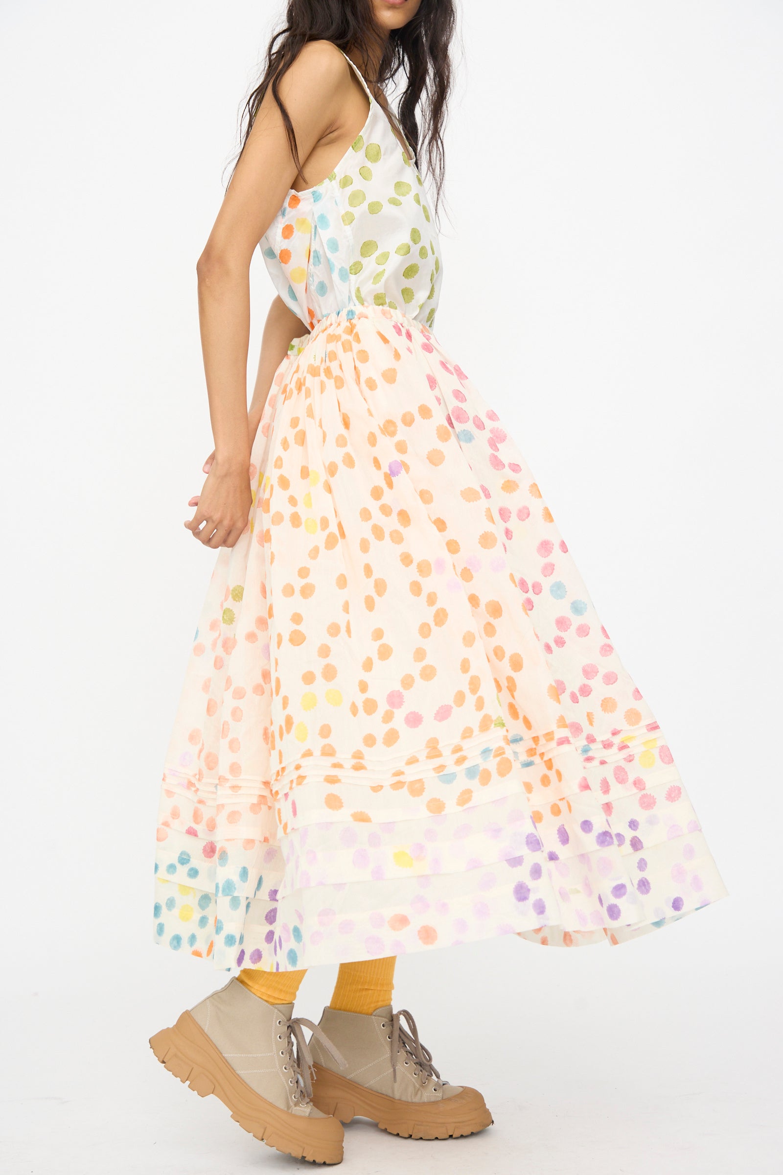 A person stands against a plain white background wearing a sleeveless leaf-patterned top and the Injiri Blockprint Silk Cotton Zamila Skirt in White Dot Multi, paired with yellow socks and beige platform boots.