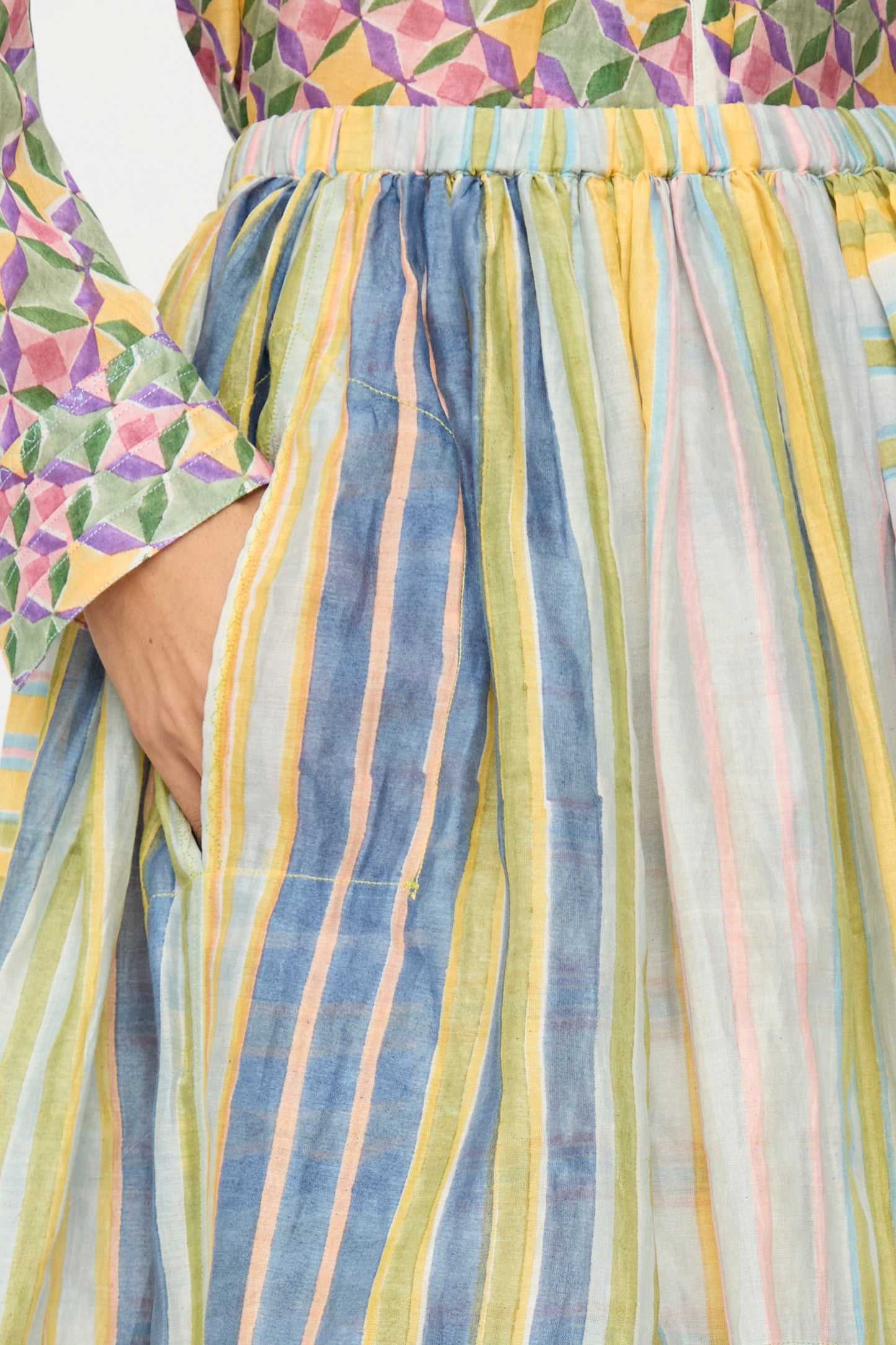 A person wearing a colorful geometric-patterned top and the Injiri Blockprint Chanderi Zamila Skirt in Green Multi, with their hand in the skirt pocket.