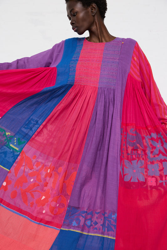 A woman models a colorful, flowing Injiri cotton dress with long sleeves, featuring vibrant shades of blue, red, and purple with floral patterns.