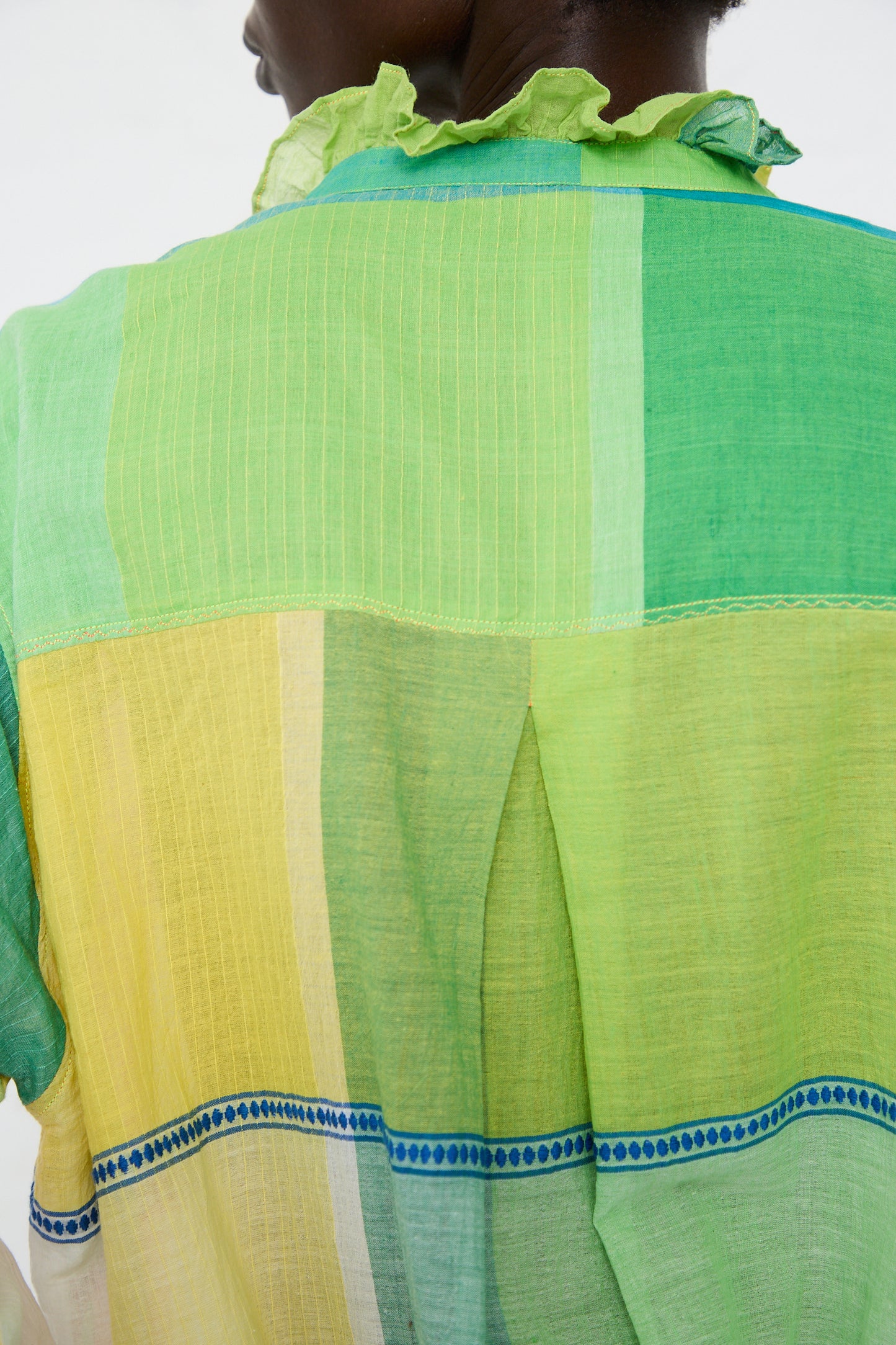 Rear view of a person wearing an Injiri relaxed fit, sheer green and yellow striped long sleeve shirt with a blue trim, focusing on the texture and colors of the fabric.