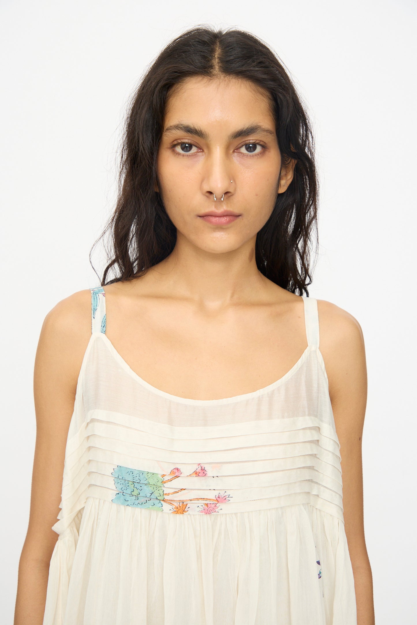 A person with long dark hair wears the Injiri Cotton Silk Blockprint Hazel Slip in White Floral, looking directly at the camera against a plain background, evoking effortless elegance.