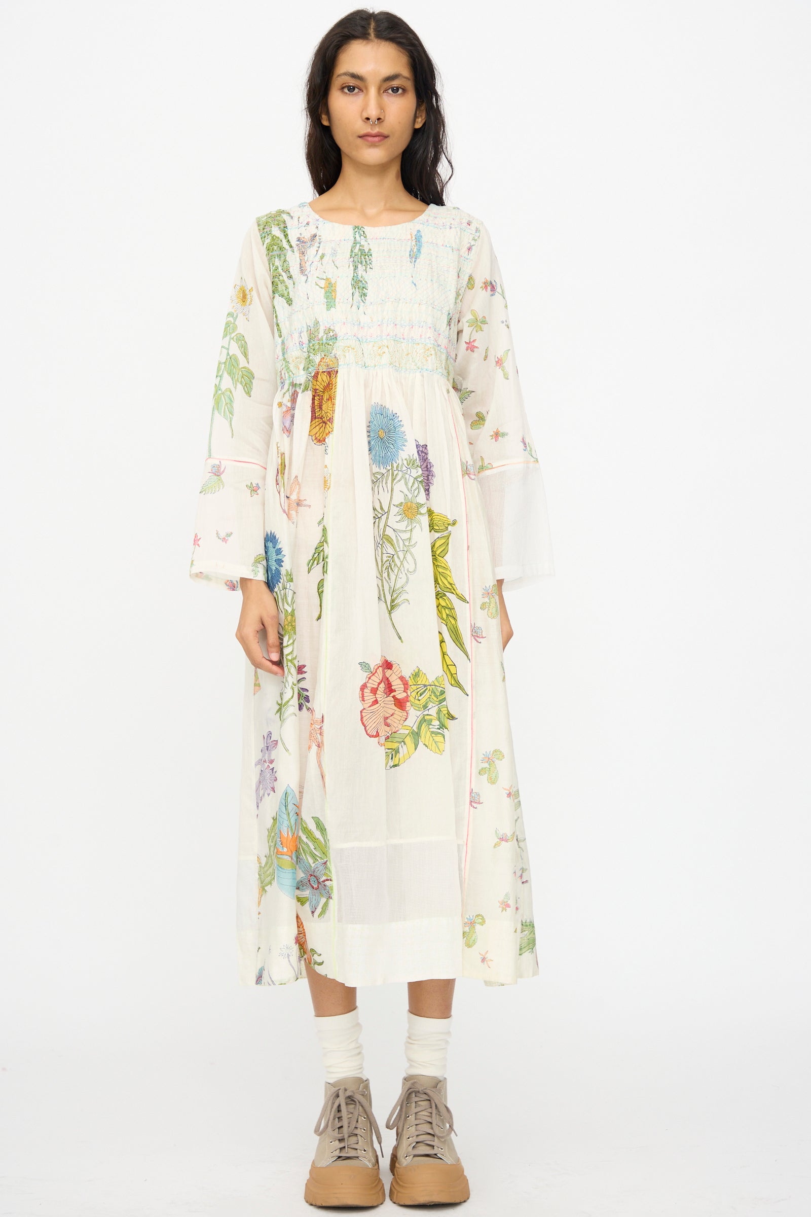 A woman faces forward against a plain white background, wearing the Injiri Cotton Silk Blockprint Nazma Dress in White, paired with light socks and tan lace-up shoes.