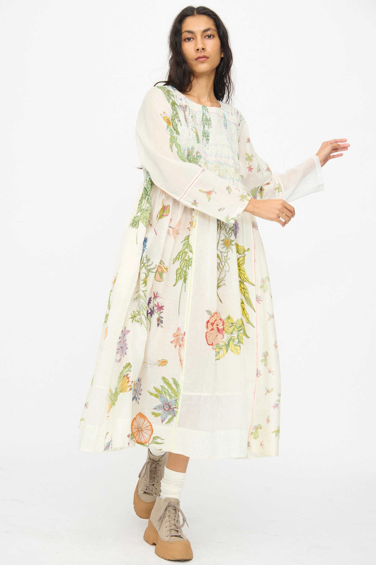 A woman wearing the Injiri Cotton Silk Blockprint Nazma Dress in White stands against a plain white background, paired with beige socks and tan shoes.